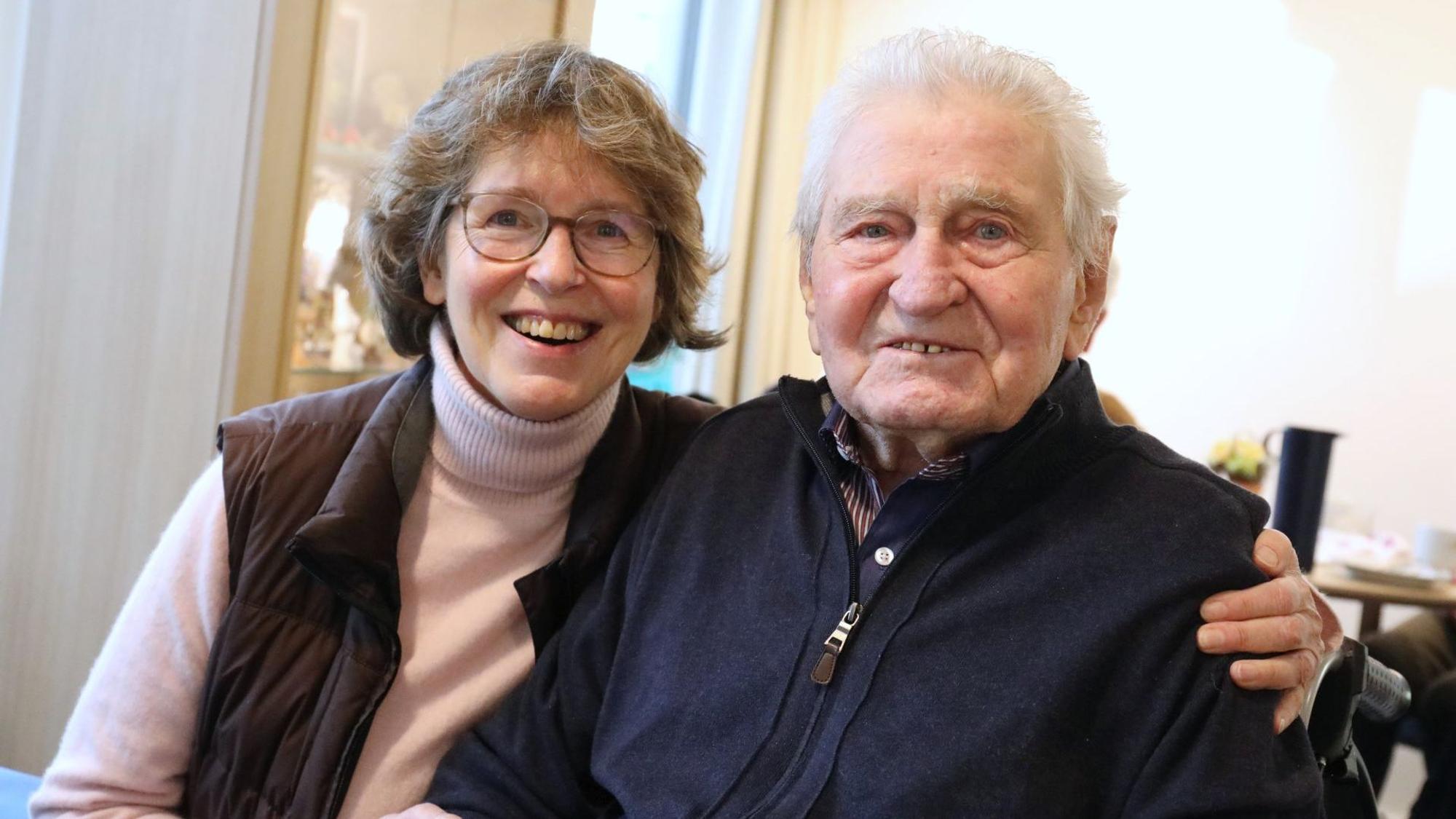 Eine Frau und ein Mann sitzen nebeneinander, sie hat einen Arm um ihn gelegt.