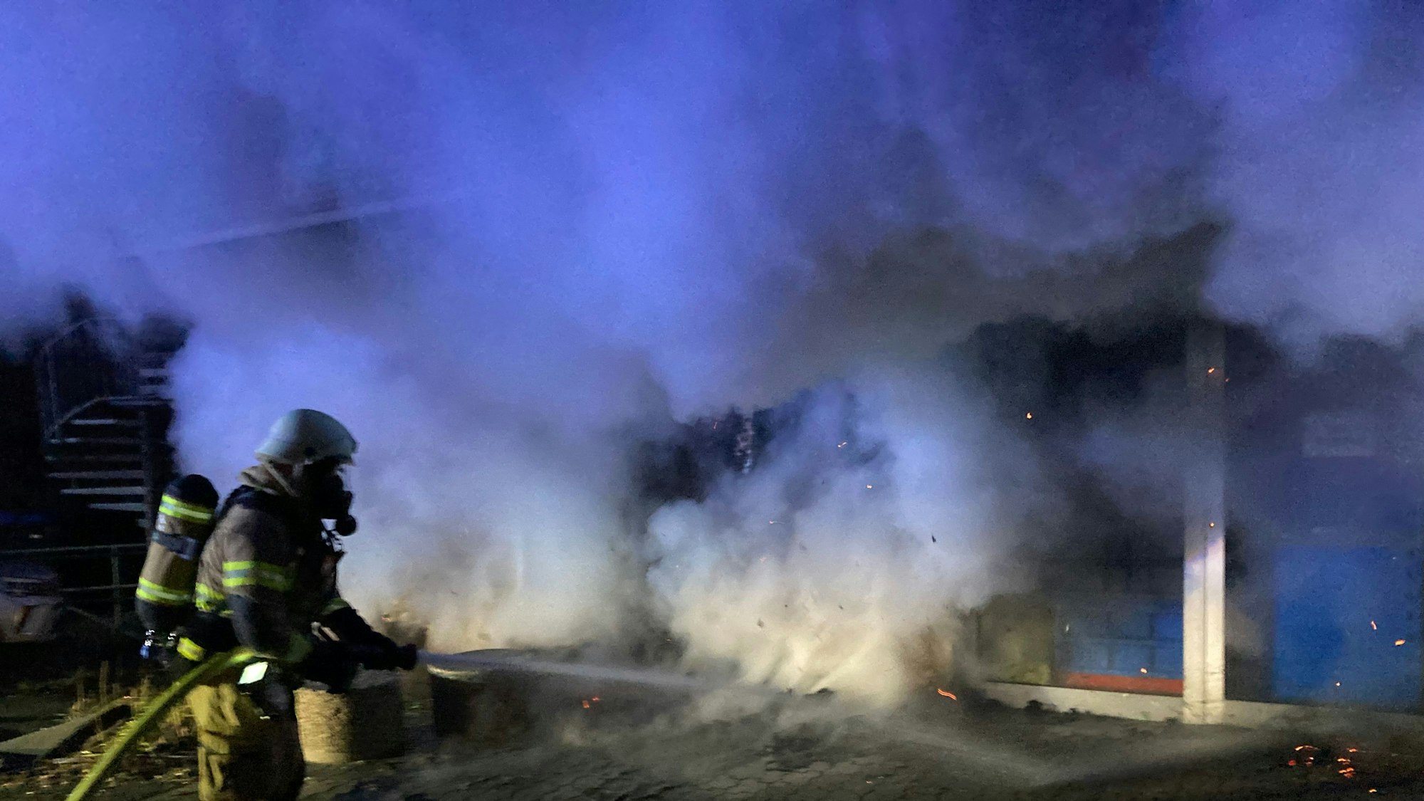 Ein Feuerwehrmann löscht einen Brand, Rauch steigt auf.