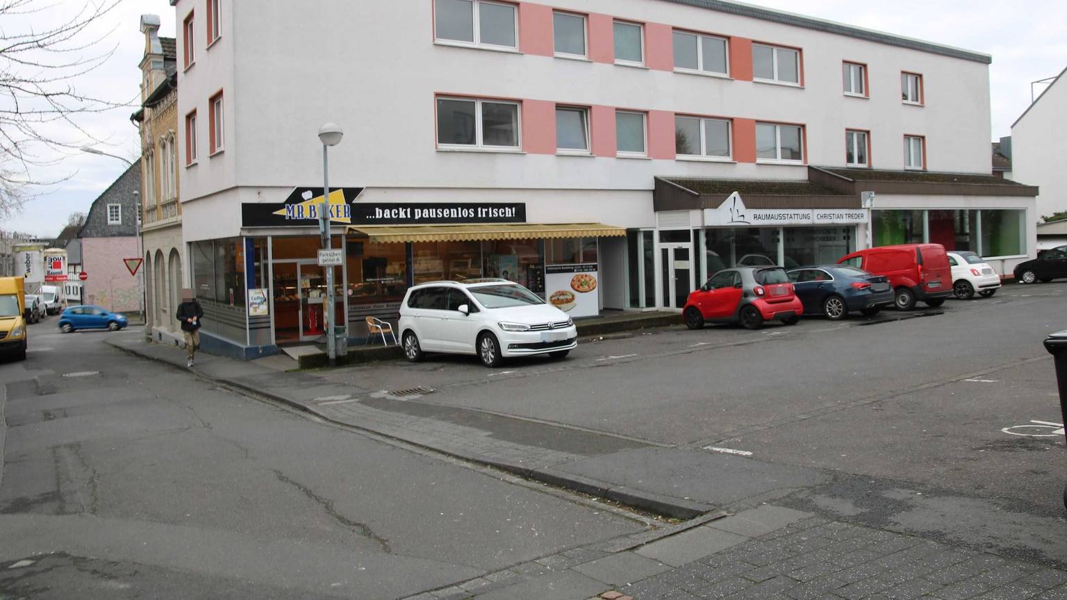 Ein dreigeschossiges Gebäude mit einem Parkplatz davor.