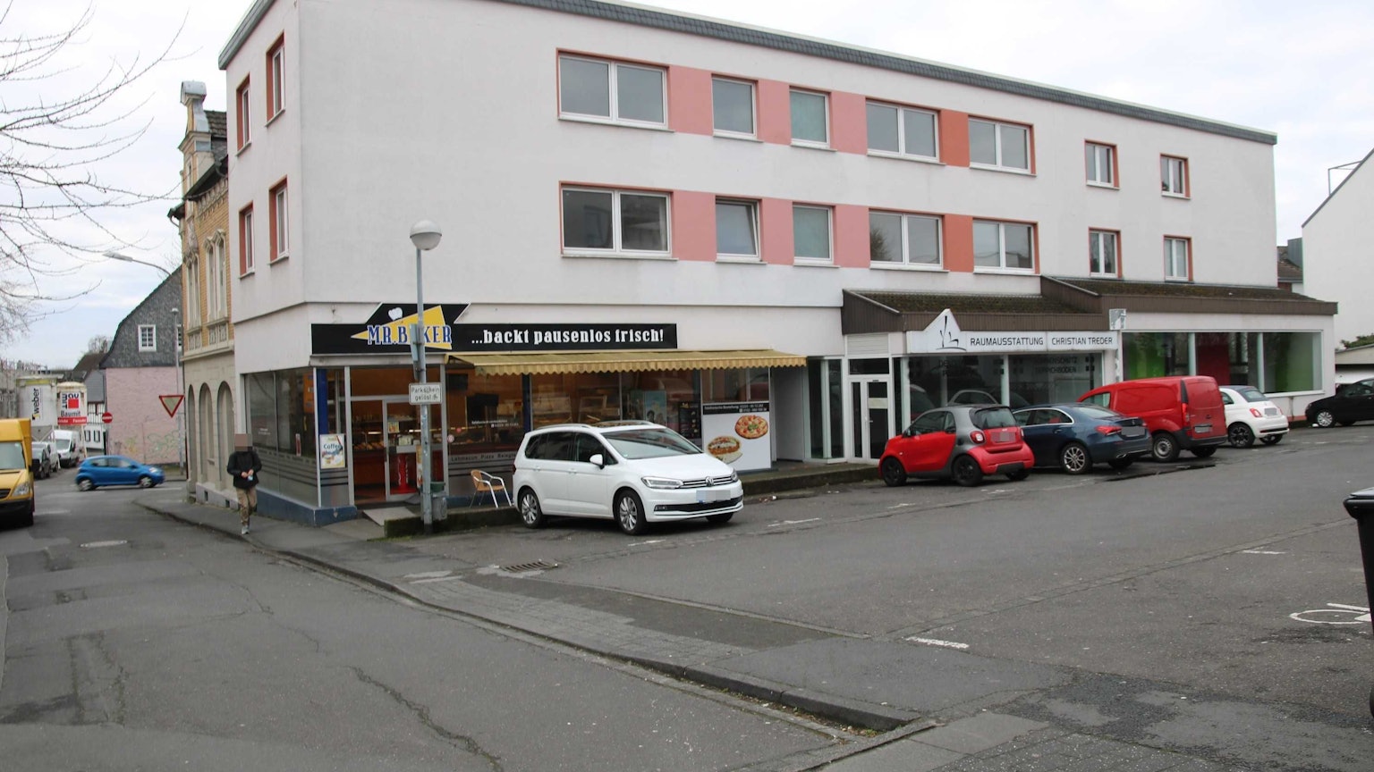 Ein dreigeschossiges Gebäude mit einem Parkplatz davor.