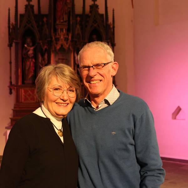 Ein Mann und eine Frau stehen vor einer rosa beleuchteten Wand und lächeln.