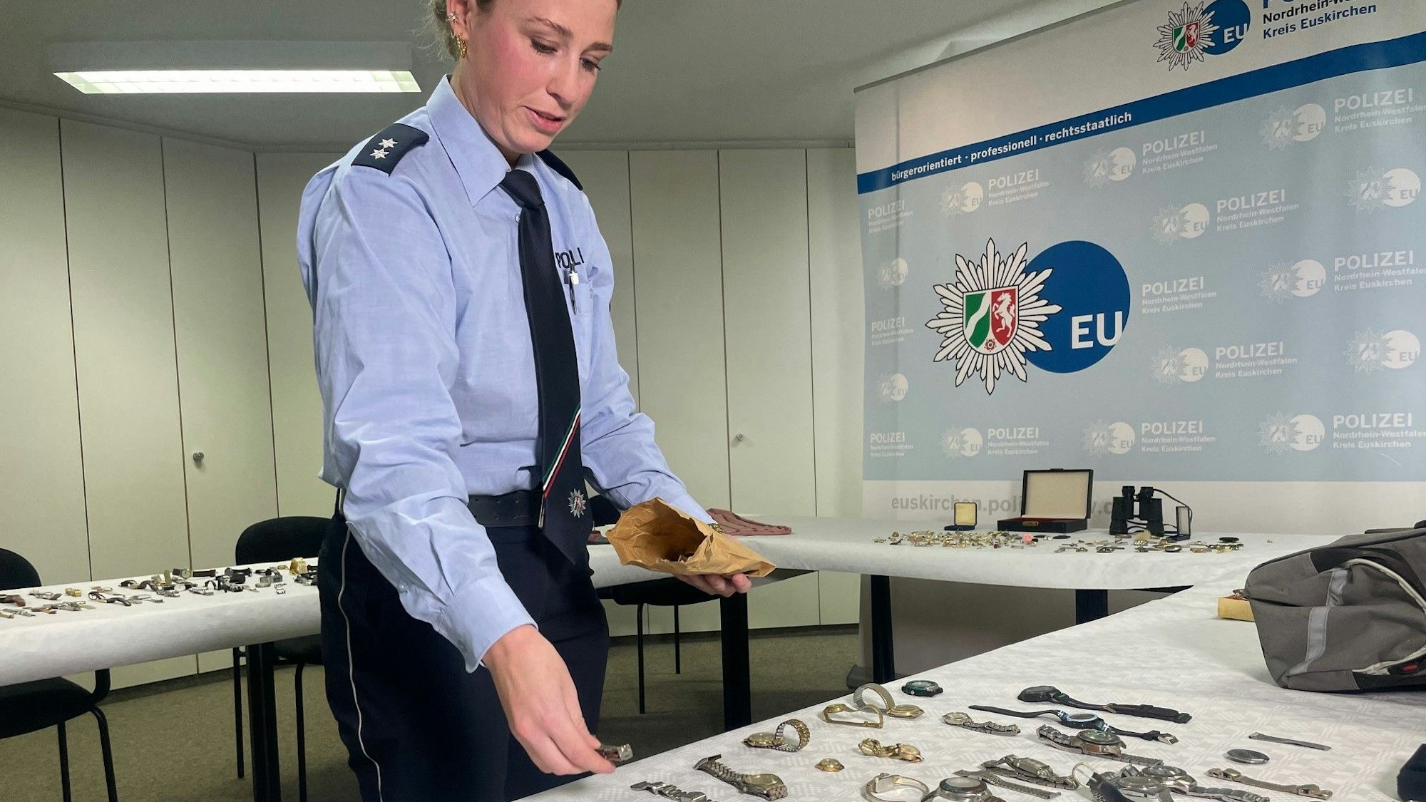 Das Bild zeigt die Beamtin, die mit ihrer rechten Hand eine Uhr auf einen Tisch legt.