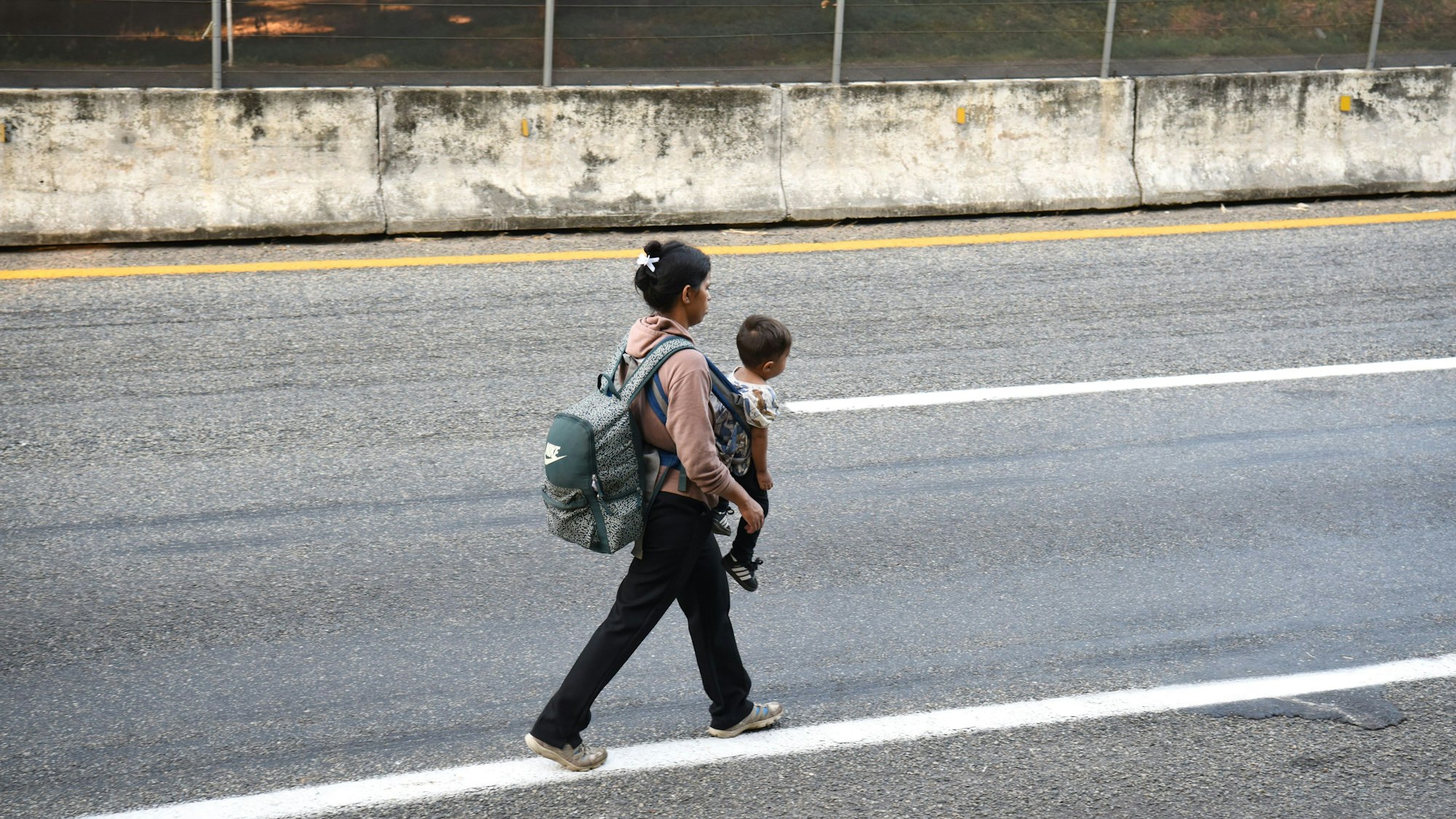 Eine Frau trägt ihr Kind am Rande einer Landstraße. Zusammen mit zahlreichen Migranten ist sie in der Nacht zuvor aus Tapachula Richtung Norden aufgebrochen.