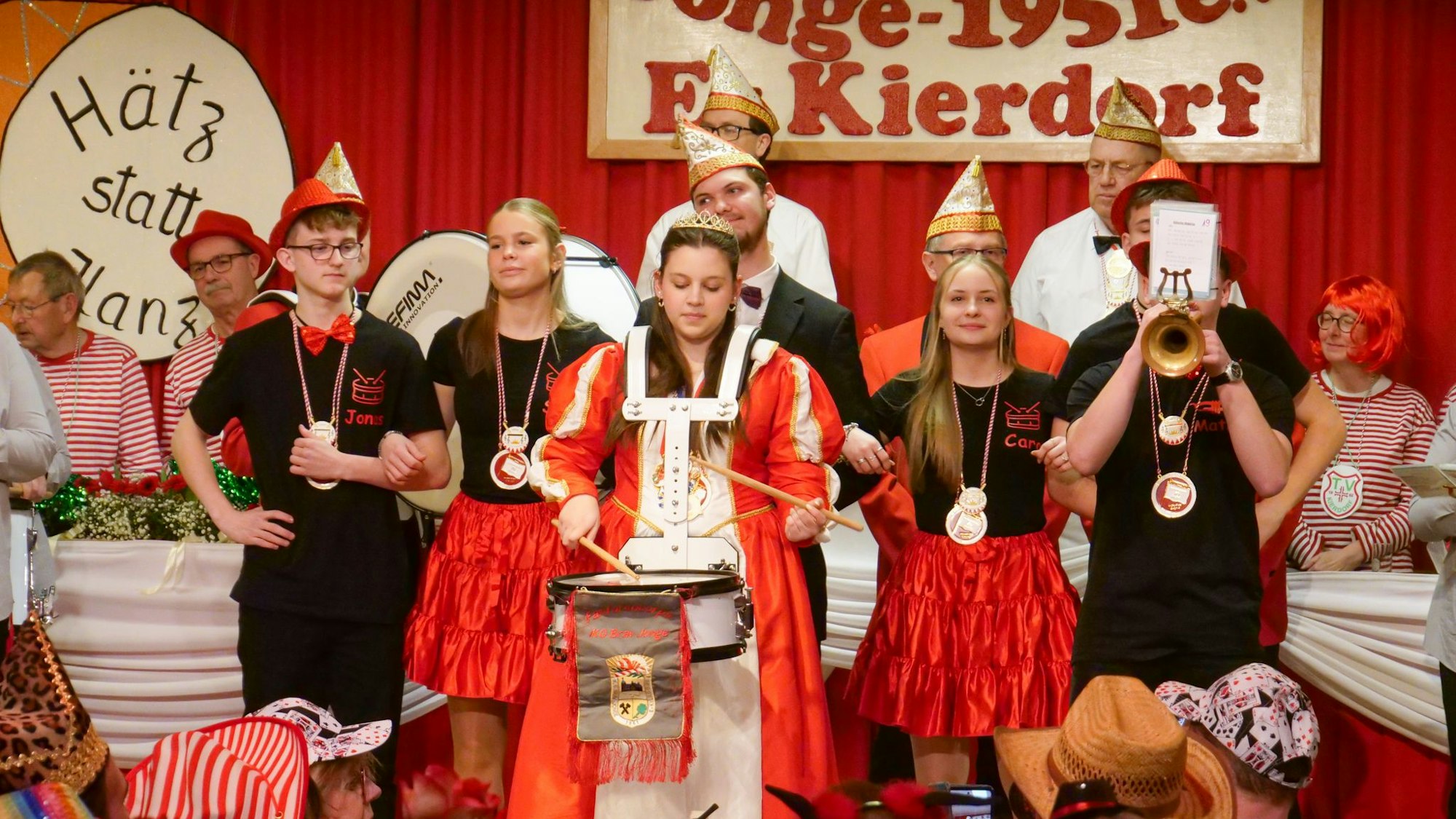 Zu sehen ist eine Karnevalsprinzessin mit Trommel und vielen anderen Menschen auf einer Bühne.