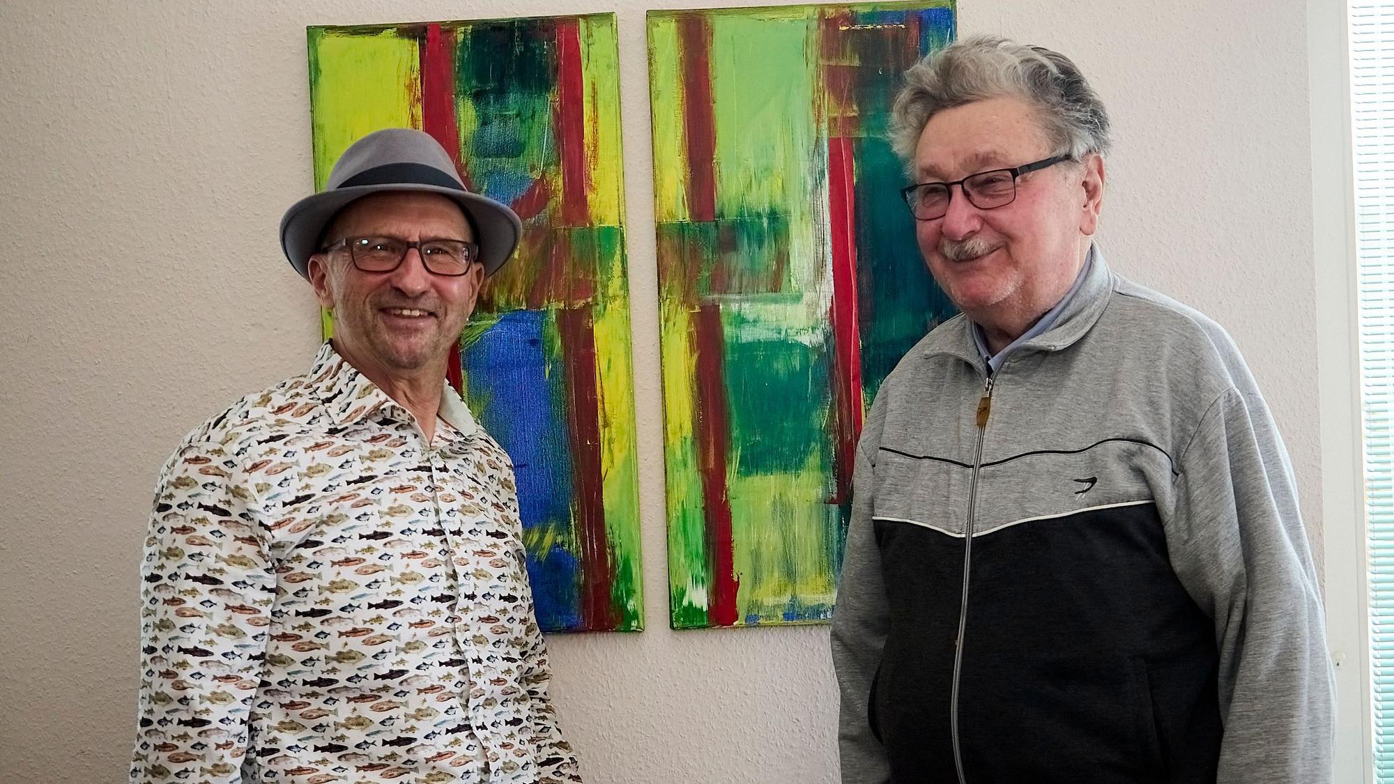 Zwei Männer, Heinz-Bert Weimbs und Albert Breuer, stehen vor einem bunten Gemälde, das an einer weißen Wand hängt.