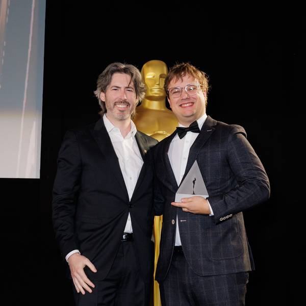 Zwei Männer vor einer großen Oscar-Statue.