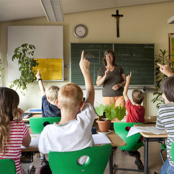 Das Foto zeigt Schüler und eine Lehrerin in einem Klassenzimmer, an der Wand hängt ein Kreuz.