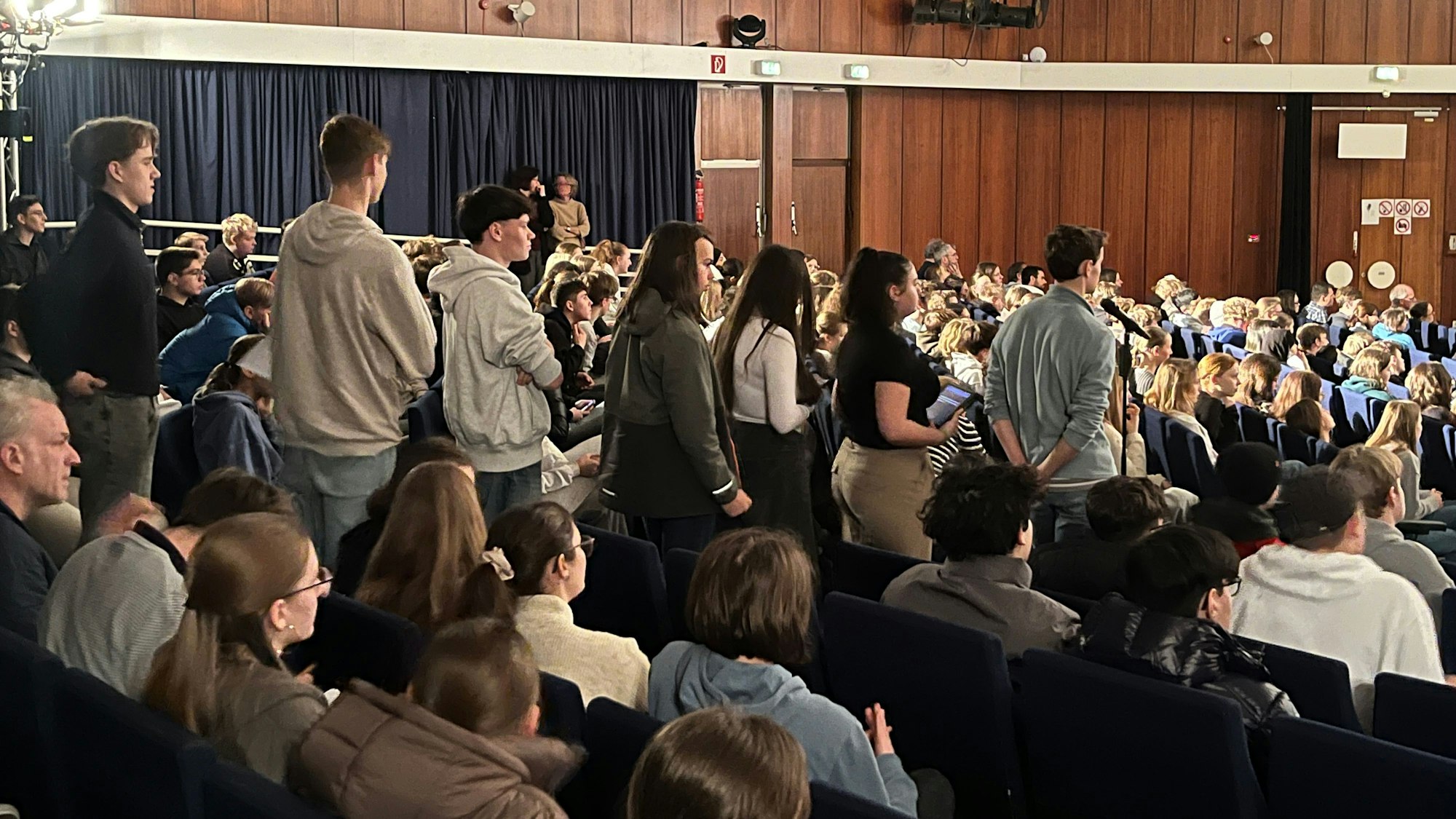 Schüler stehen in einer Aula Schlange vor einem Mikrofon.