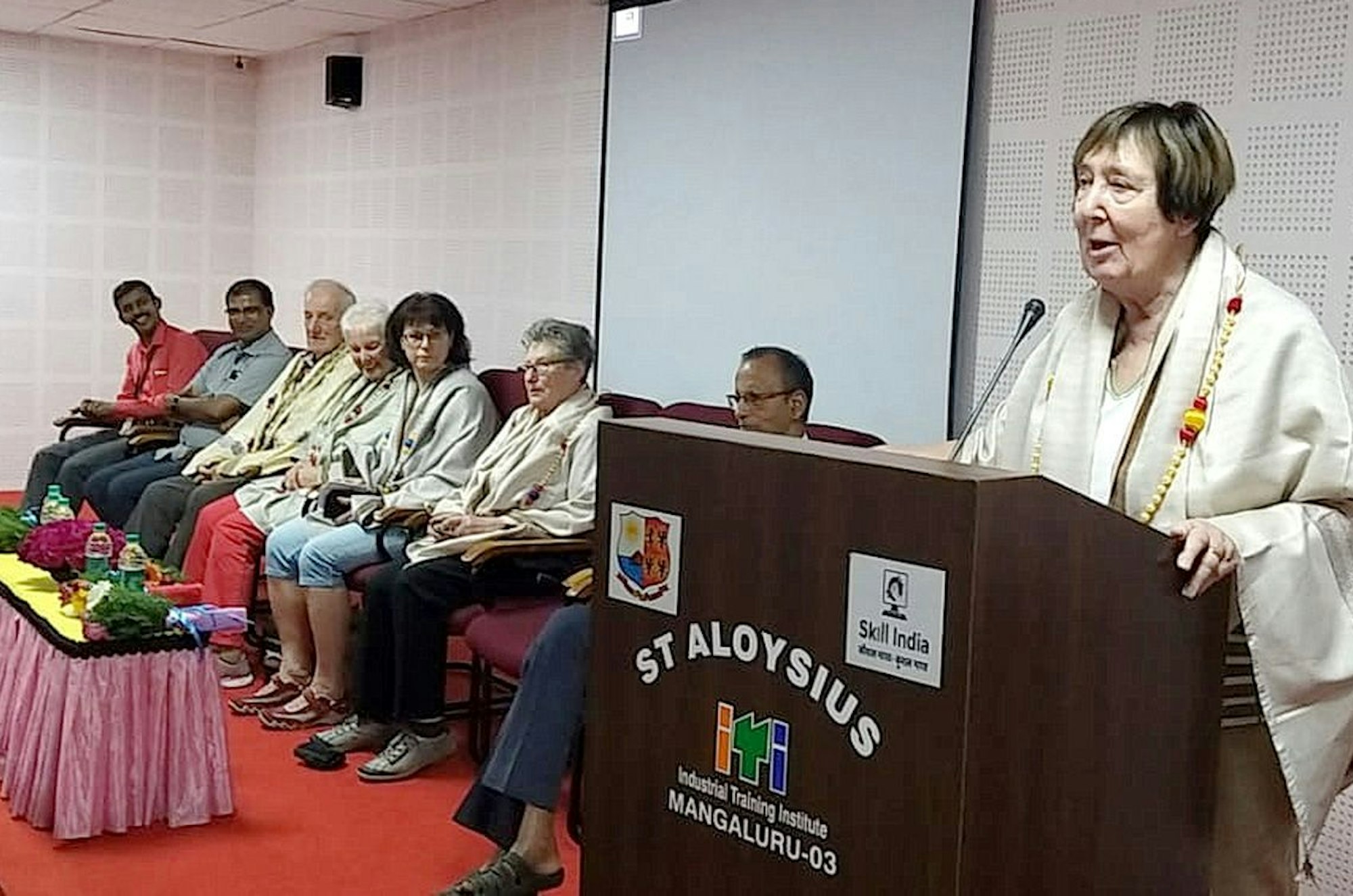 Anneliese Klinkhammer (r.) steht bei einem Besuch in Indien am Rednerpult; im Hintergrund sind weitere Mitglieder einer Besuchergruppe zu sehen.