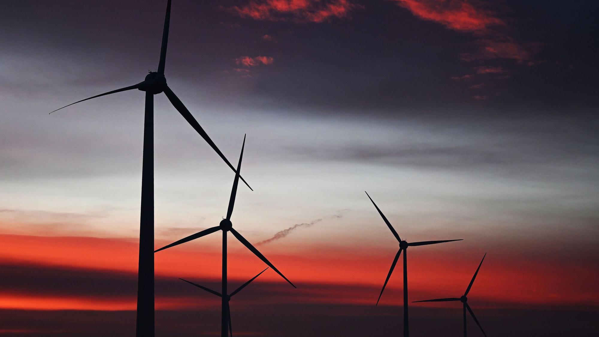 Zu sehen sind mehrere Windräder bei Sonnenaufgang.