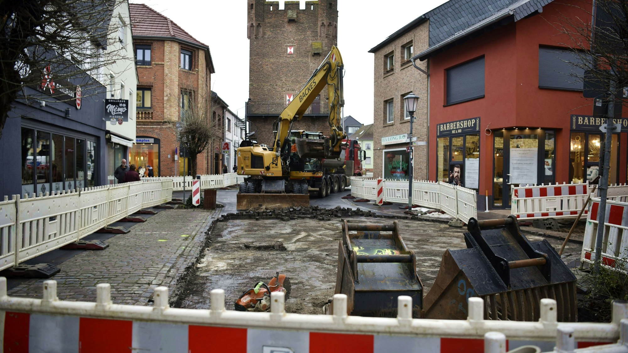 Ein gelber Bagger baggert vor der Kulisse des Münstertors das Kopfsteinpflaster auf der Münsterstraße auf. Drumherum stehen rot-weiße Warnbaken.
