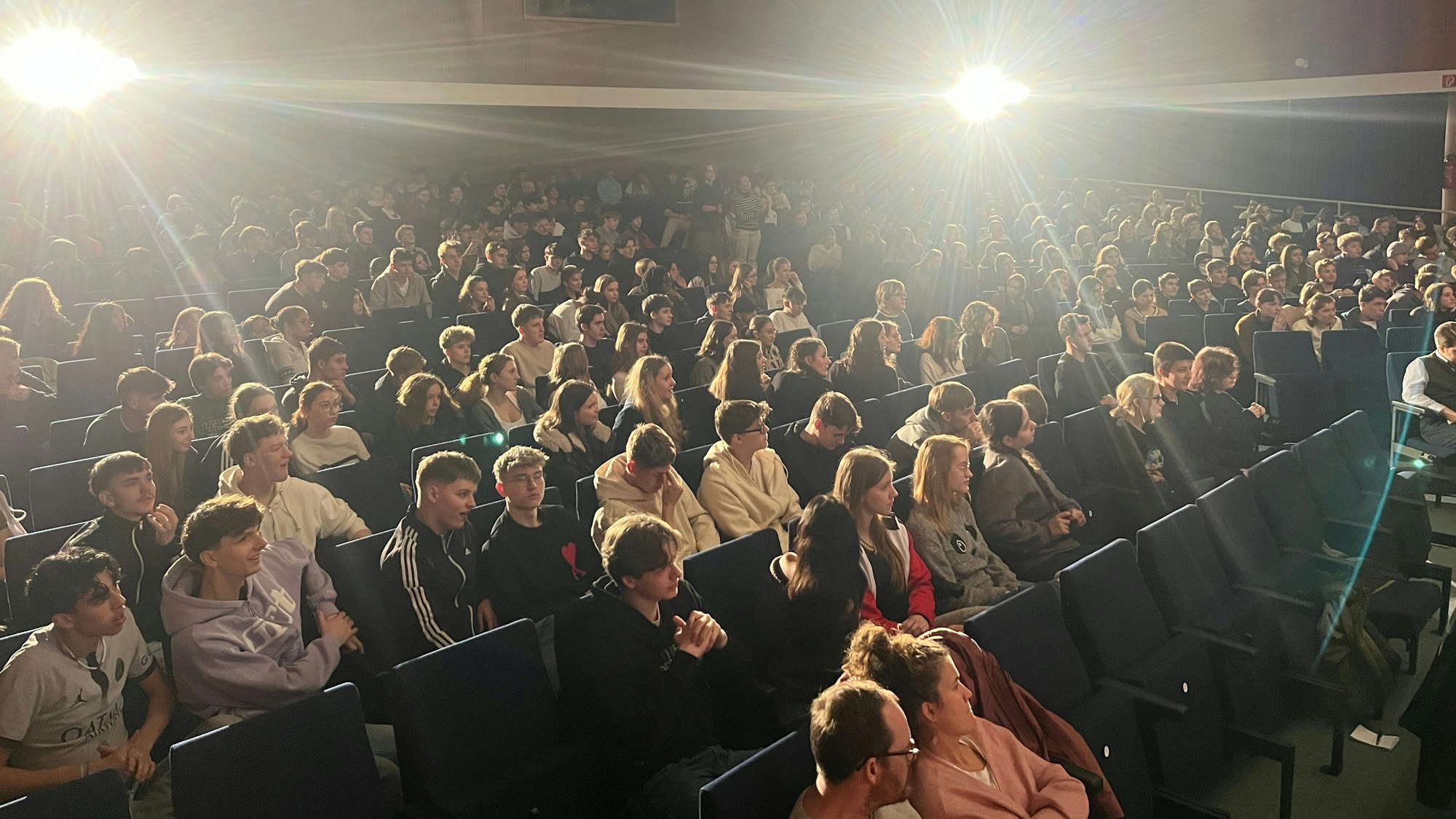 Schüler sitzen auf Stühlen in einer Aula.