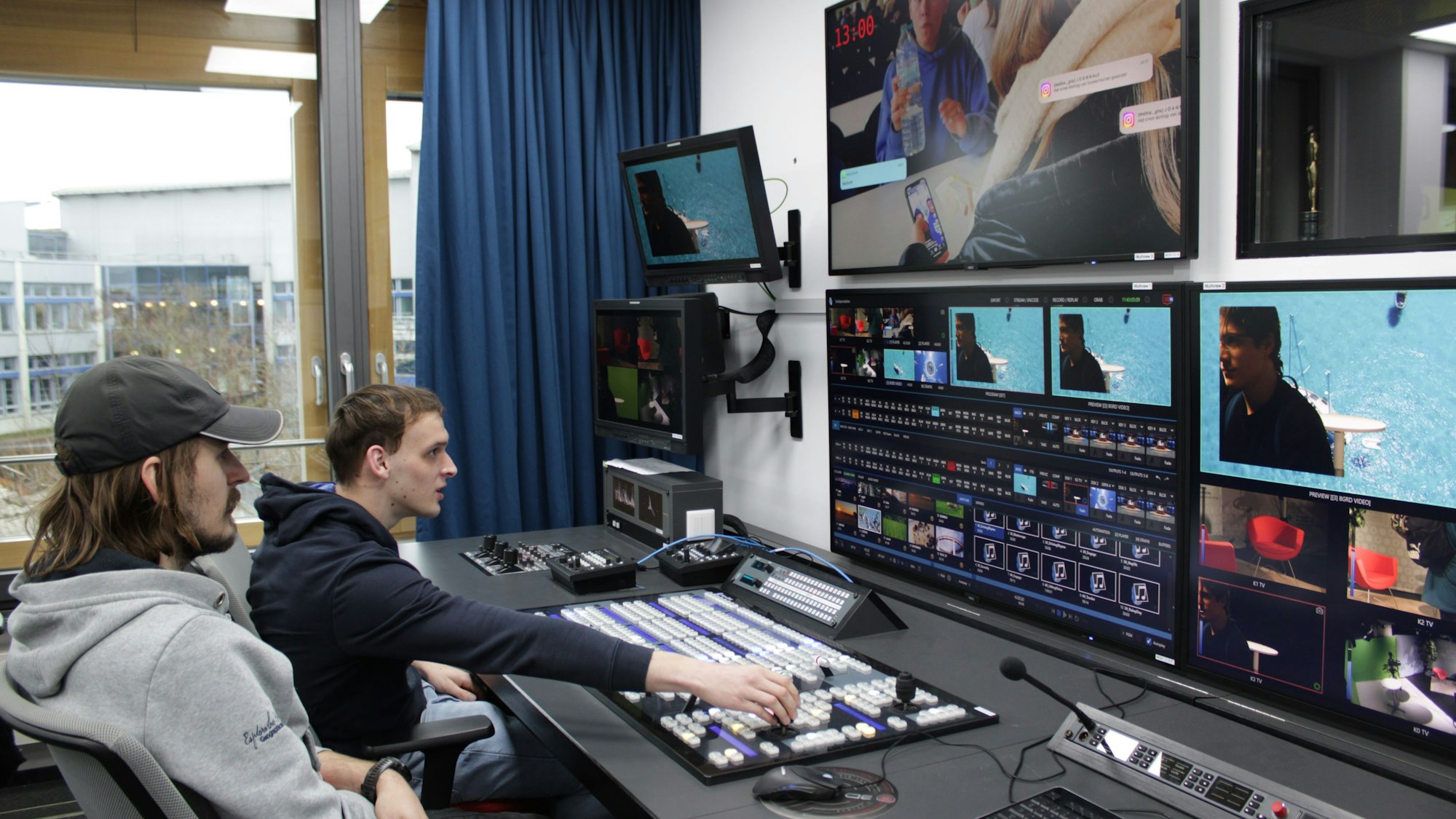 Zwei Studenten sitzen vor drei großen Bildschirmen und arbeiten mit einem Schnittprogramm.