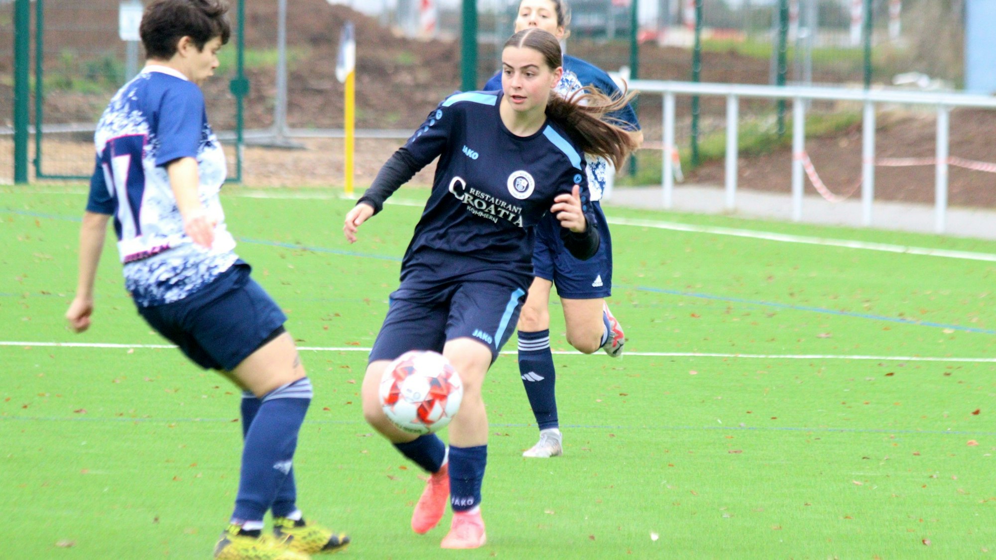 Eine junge Frau dribbelt in dunkelblauem Trikot eine Gegenspielerin aus.
