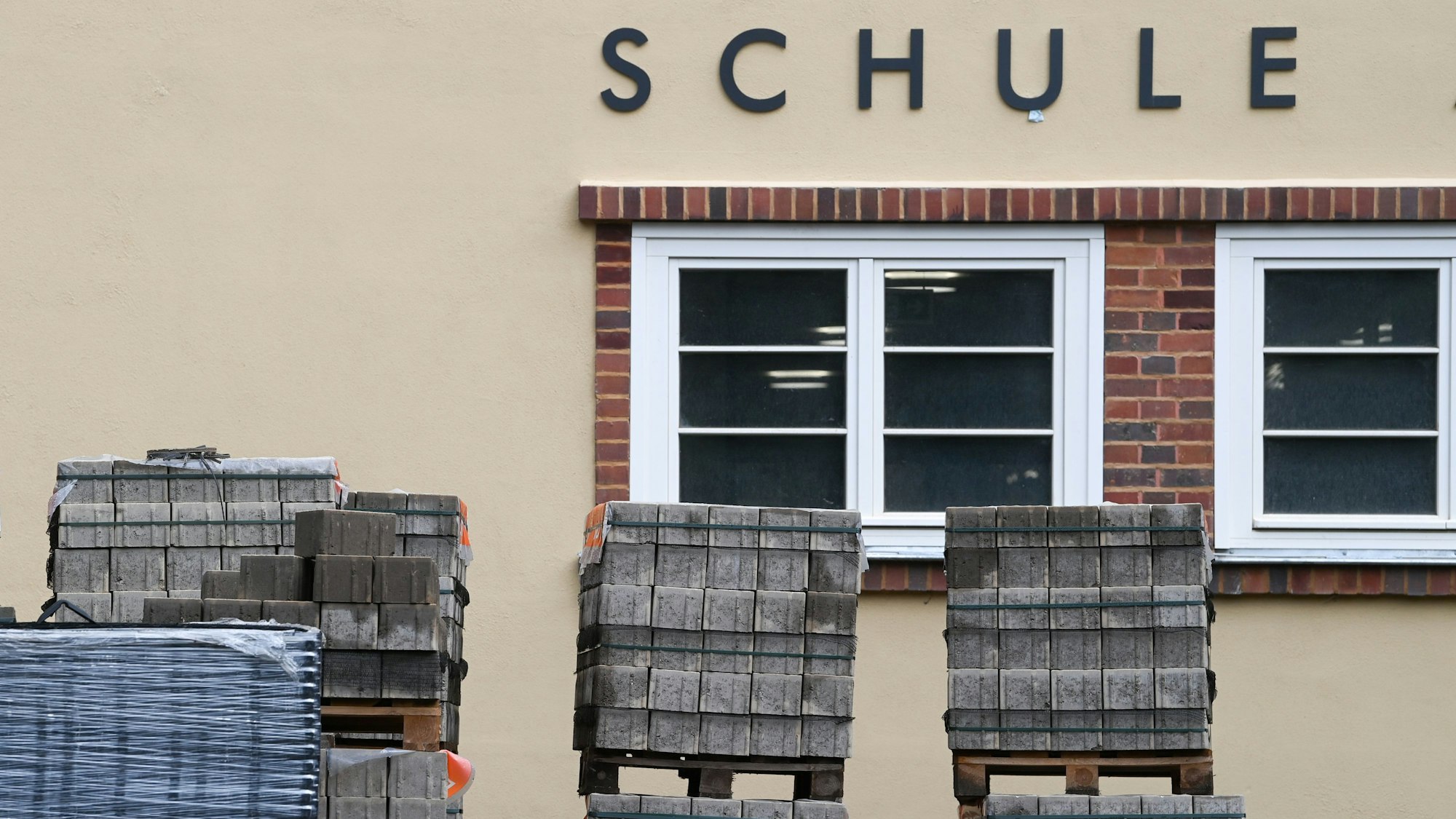 Zu sehen ist die Fassade eines Schulgebäudes. Davor steht Baumaterial.