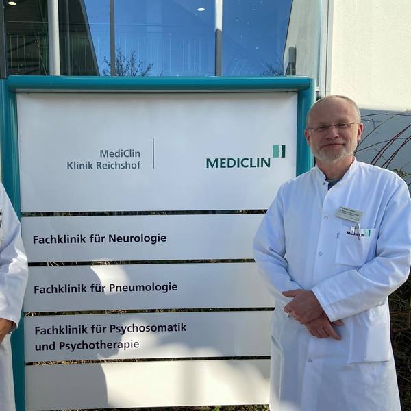 Matthias Schmalenbach, Chefarzt der Pneumologie an der Mediclin-Rehaklinik in Reichshof-Eckenhagen, und Jürgen Bonnert, Chefarzt der Neurologie und kommissarischer Chefarzt für Psychosomatik und Psychotherapie, stehen vor einem Klinikschild.