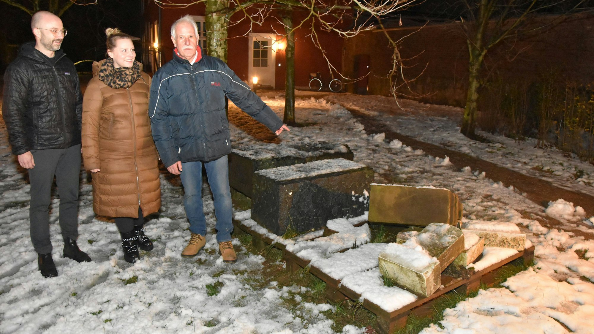 Zu sehen sind zwei Männer und eine Frau vor umgeworfenen Grabsteinen.