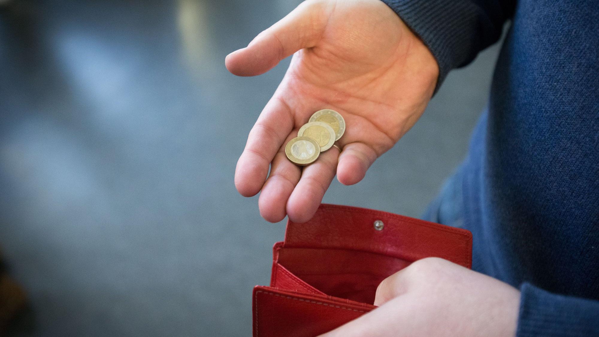Münzen im Wert von fünf Euro werden in Paderborn über ein rotes Portemonnaie gehalten.