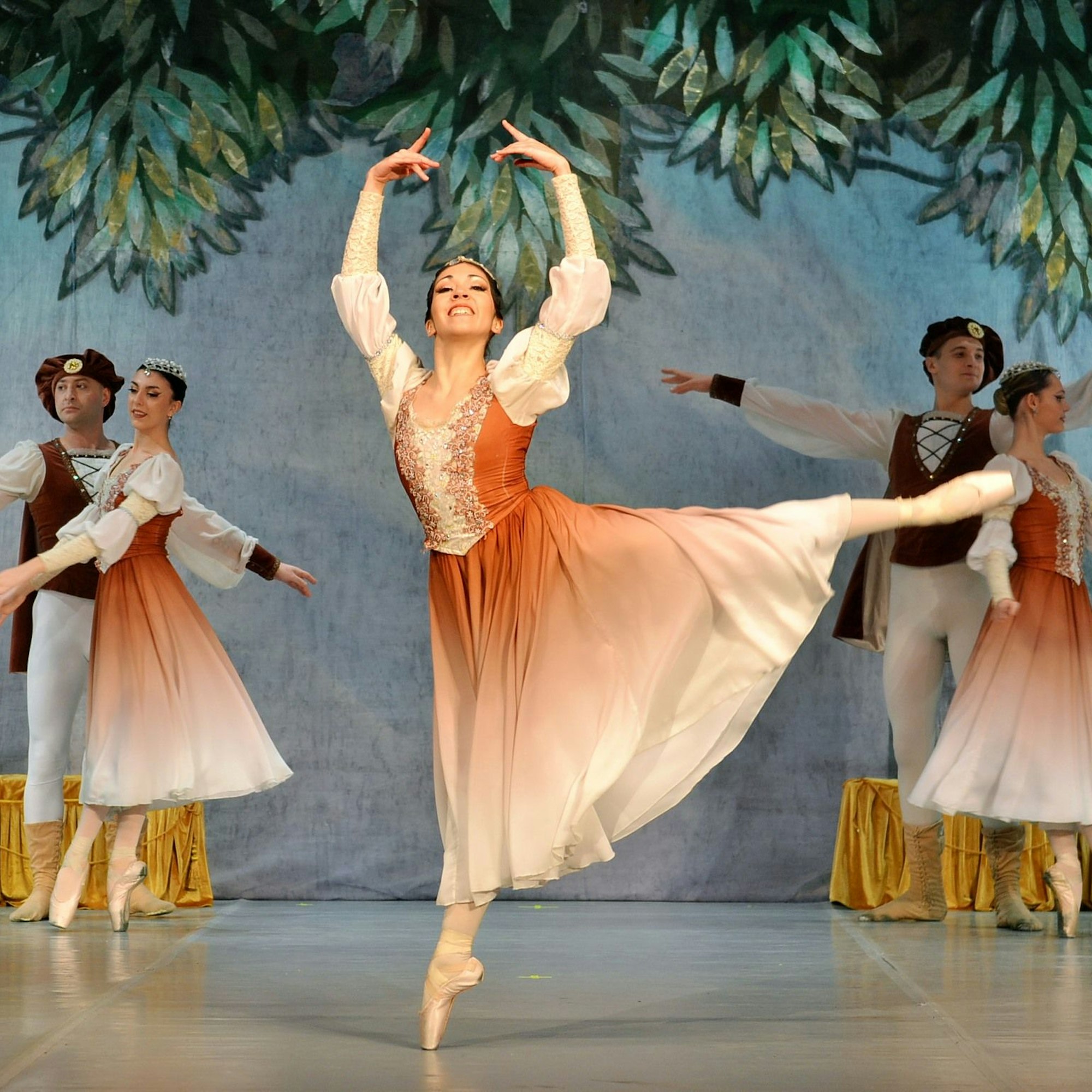 Eine Balletttänzerin in einem orange-weißen Kleid tanzt auf einer Bühne.