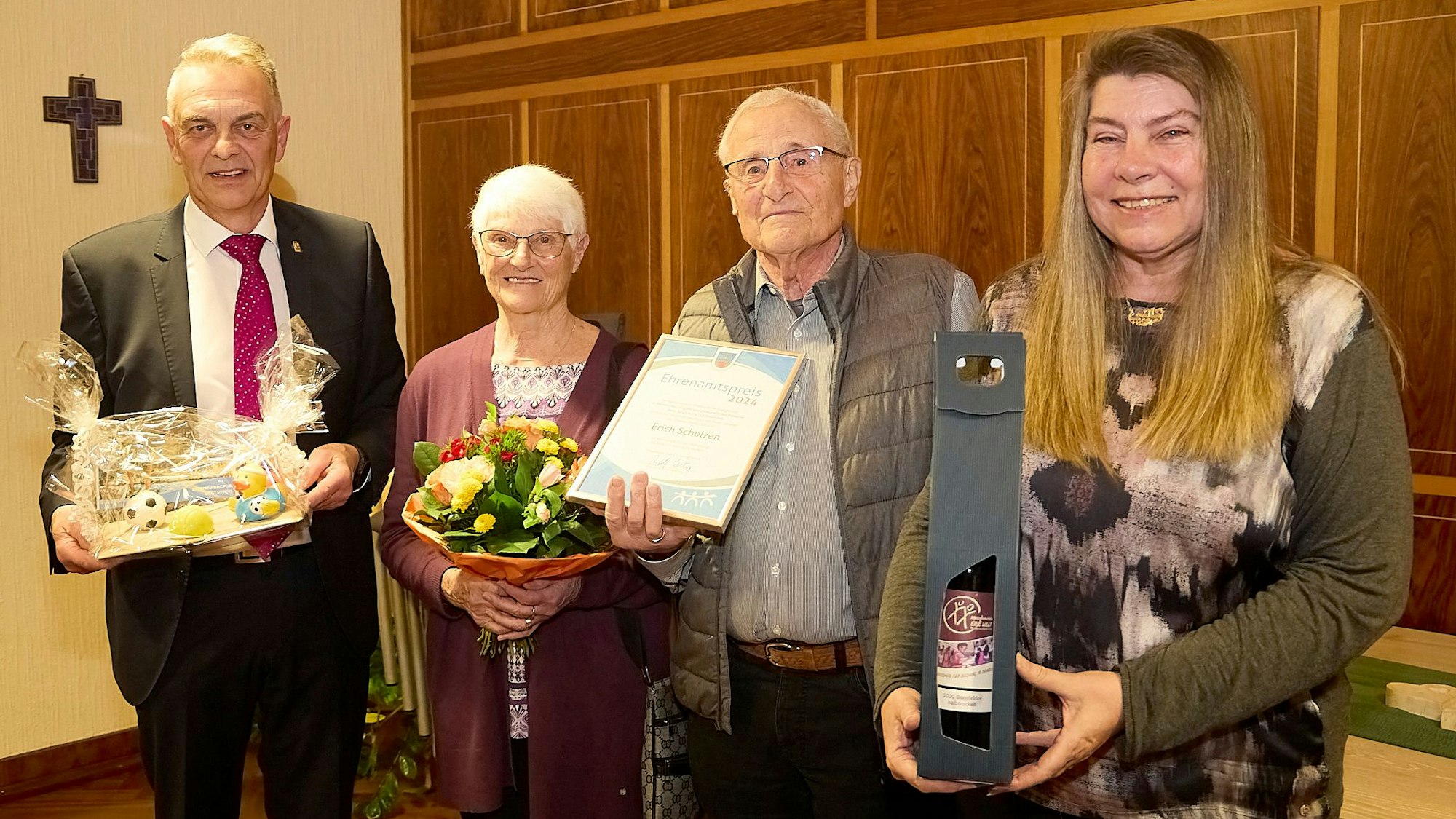 Erich Scholzen steht neben seiner Frau Marlene, dem Bürgermeister Rudolf Westerburg (links) und Katharina Koenn (rechts). Scholzen hält eine Urkunde in den Händen, seine Frau einen Blumenstrauß.