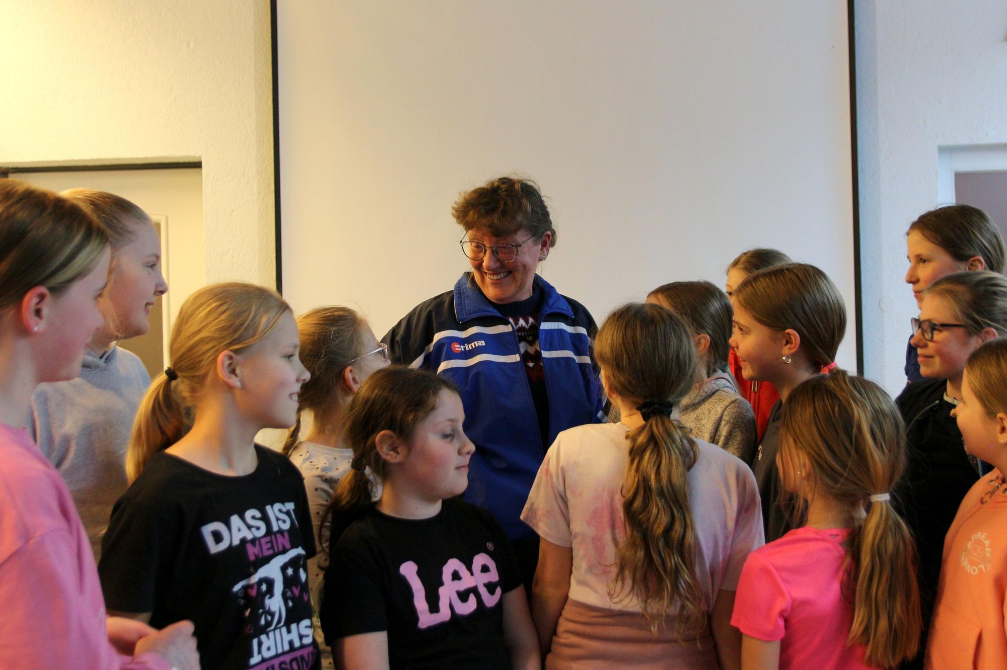 Auf dem Bild ist eine Frau inmitten von Kindern beim Tanztraining zu sehen.