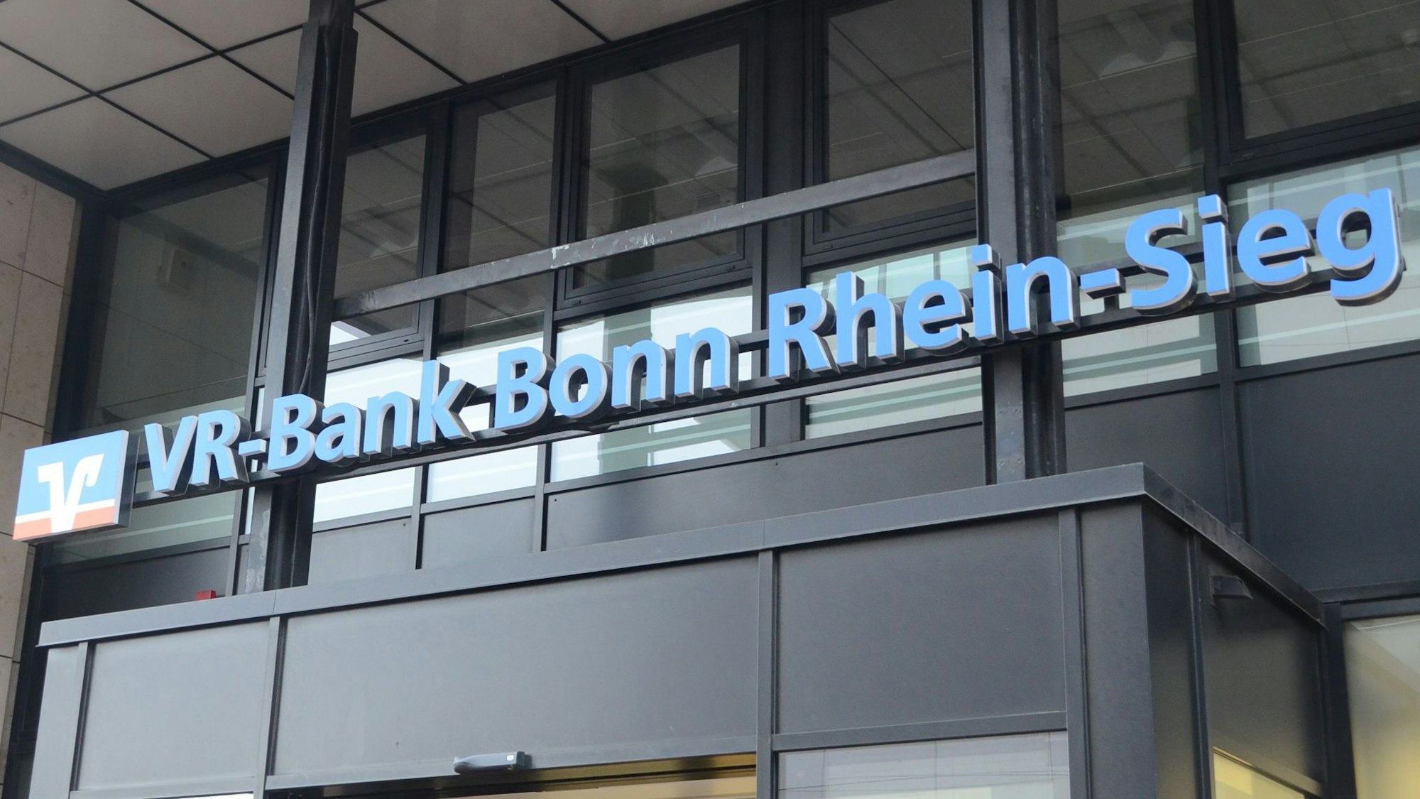 Der Schriftzug VR-Bank Bonn Rhein-Sieg über dem Eingang einer Bankfiliale.