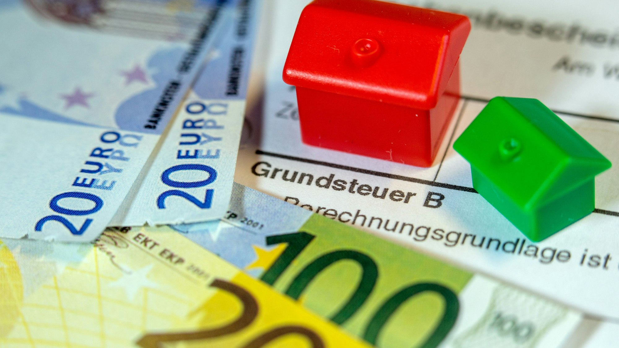 Das Symbolfoto zeigt zwei Spielhäuschen, Geldscheine und ein Formular mit der Aufschrift "Grundsteuer B".