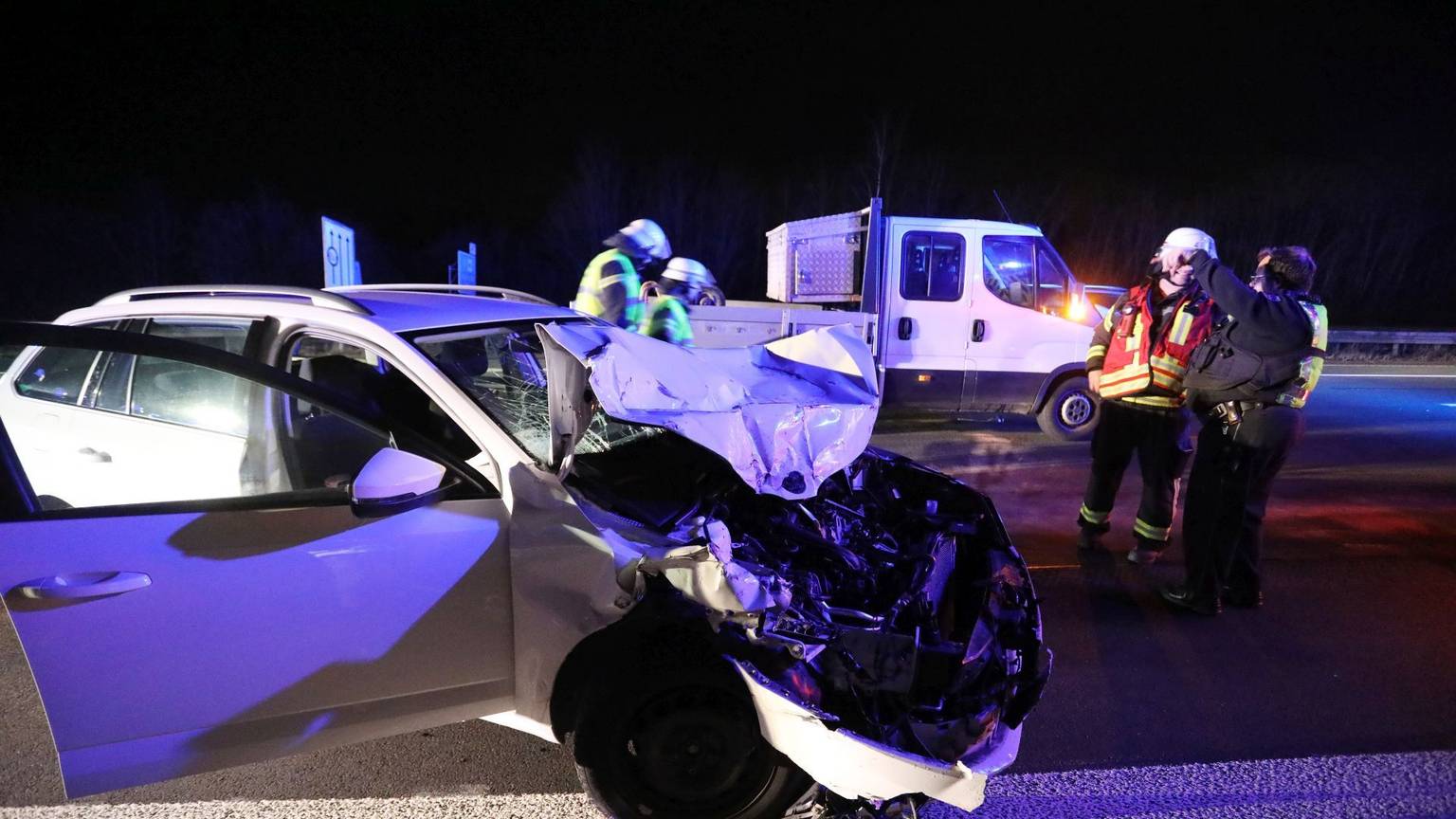 Feuerwehrleute stehen neben einem Auto mit demolierter Front