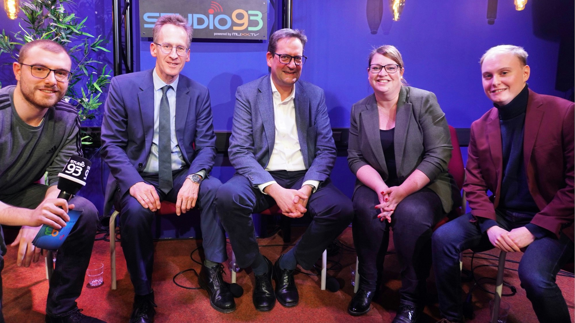 Vier Männer und eine Frau sitzen in einem Studio.