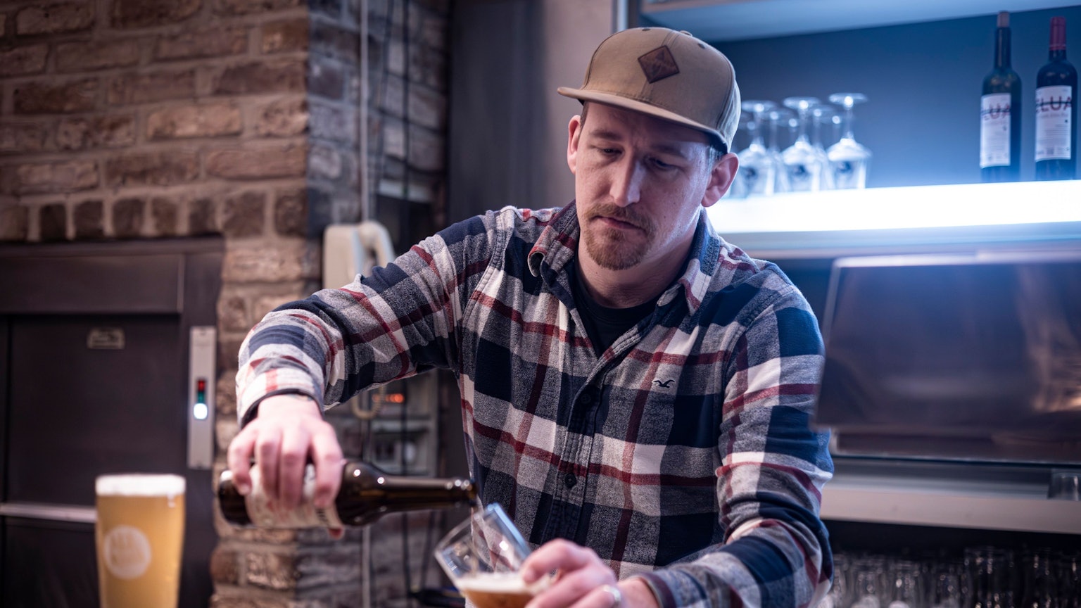 Balthasar Fischer hinter der Theke, er schenkt Bier aus einer Flasche ins Glas.