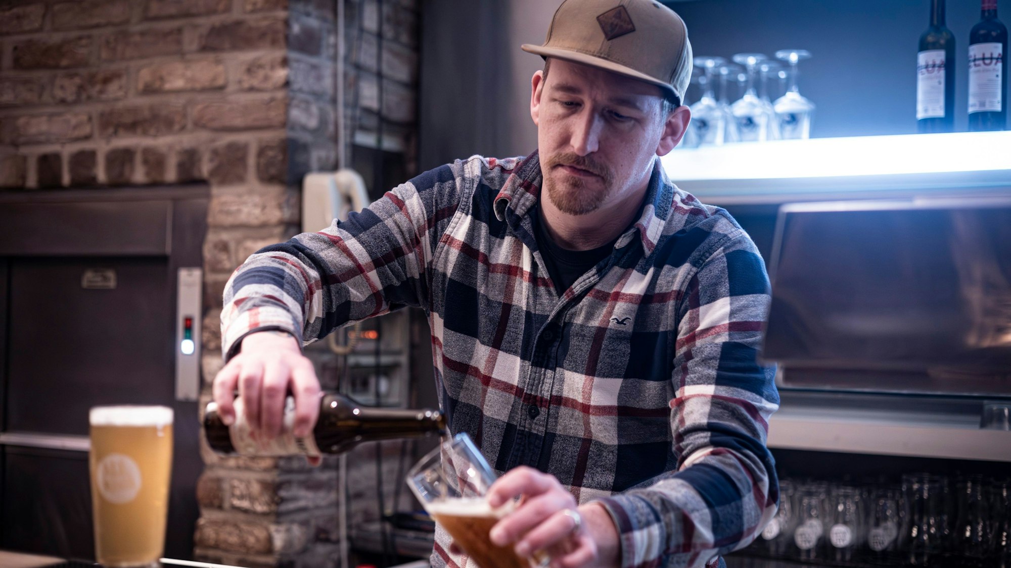Balthasar Fischer hinter der Theke, er schenkt Bier aus einer Flasche ins Glas.