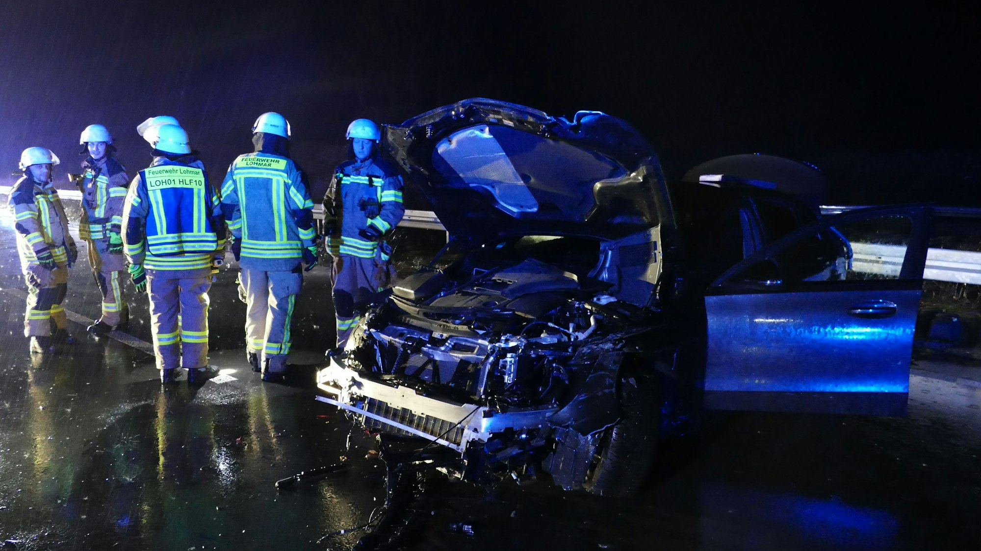 Feuerwehrleute in der Nacht neben einem stark beschädigten PKW.