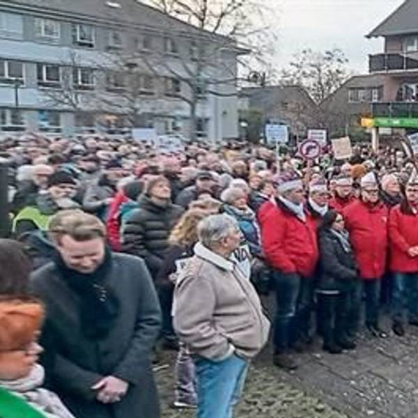 Menschen stehen auf einem Platz. Einige tragen Protestschilder.