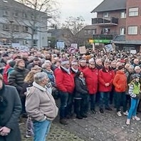 Menschen stehen auf einem Platz. Einige tragen Protestschilder.
