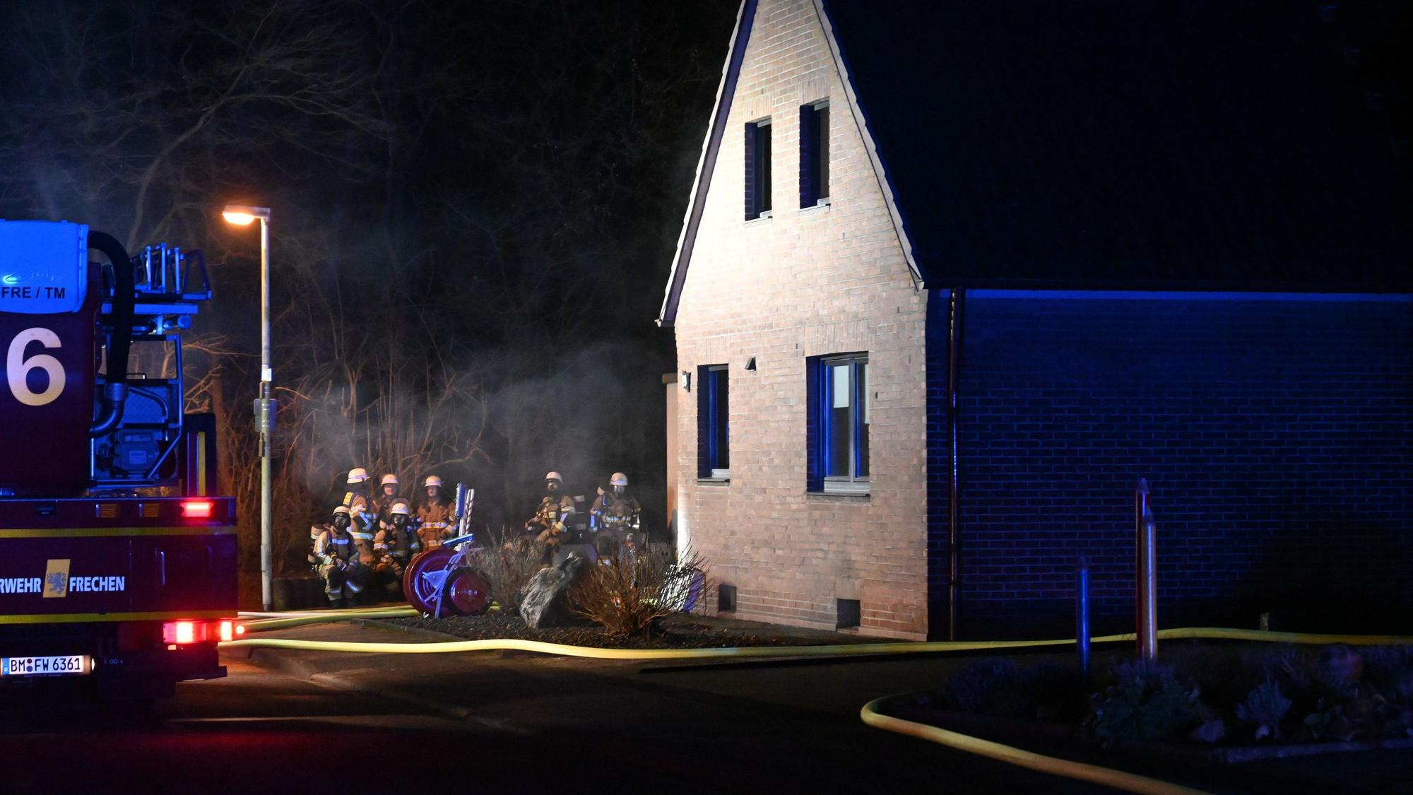 Feuerwehrleute, ein Einsatzfahrzeug und ein gelber dicker Schlauch sind vor einem Einfamilien
