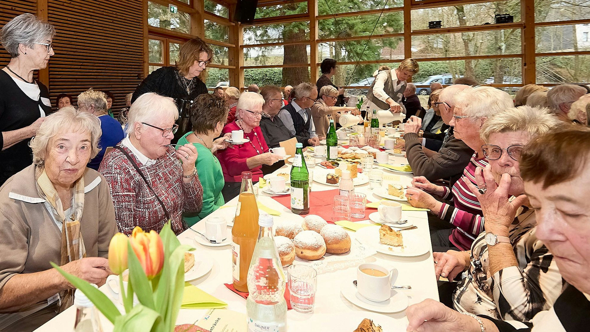 An einem langen Tisch, der eingedeckt ist, sitzen Seniorinnen und Senioren.