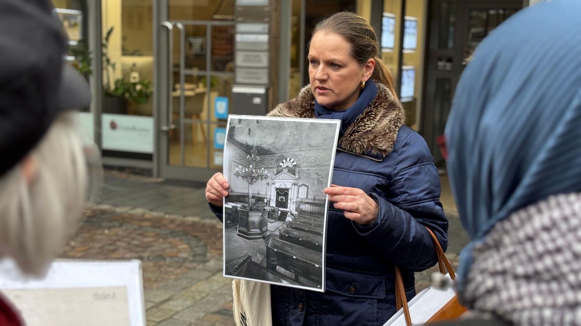Eine Frau hält eine Schwarz-Weiß-Aufnahme vor sich, auf der der Innenraum einer Synagoge abfotografiert wurde.
