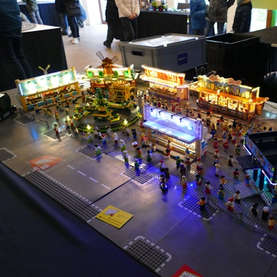 Ein Kirmesgelände aus Klemmbausteinen, beleuchtet und bevölkert mit kleinen Spielfiguren.
