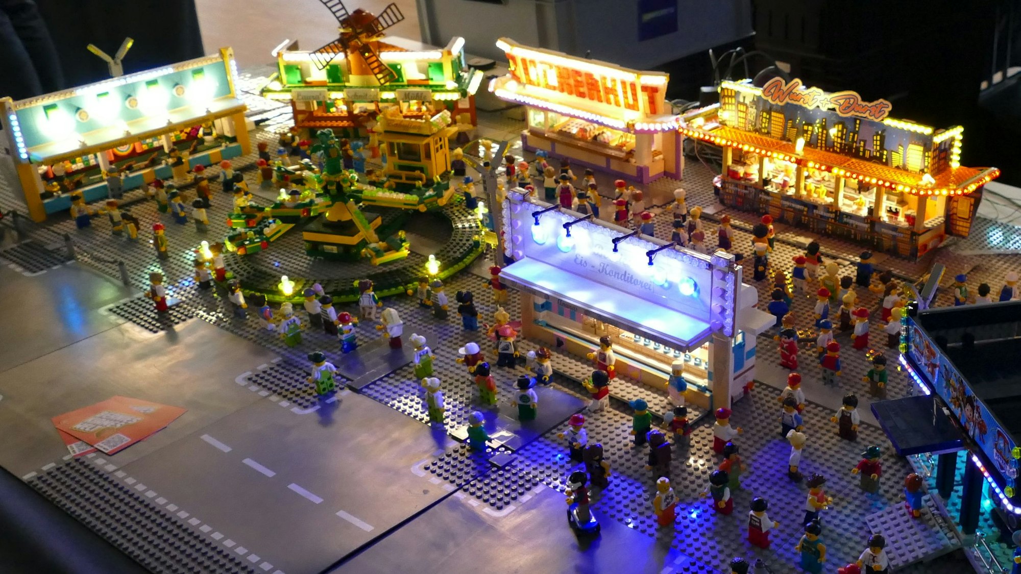 Ein Kirmesgelände aus Klemmbausteinen, beleuchtet und bevölkert mit kleinen Spielfiguren.