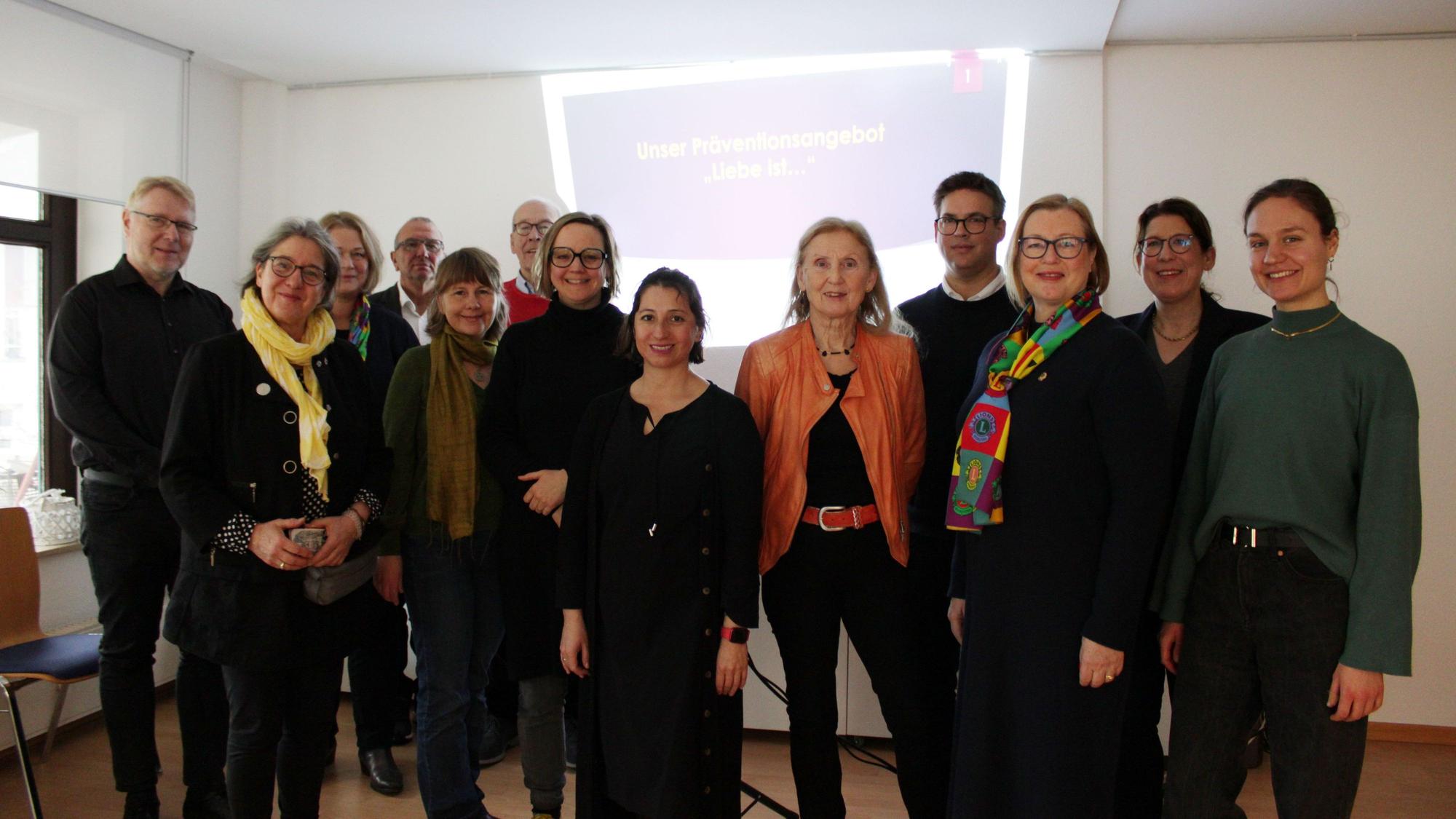 Männer und Frauen stehen vor einer Beamer-Projektion.