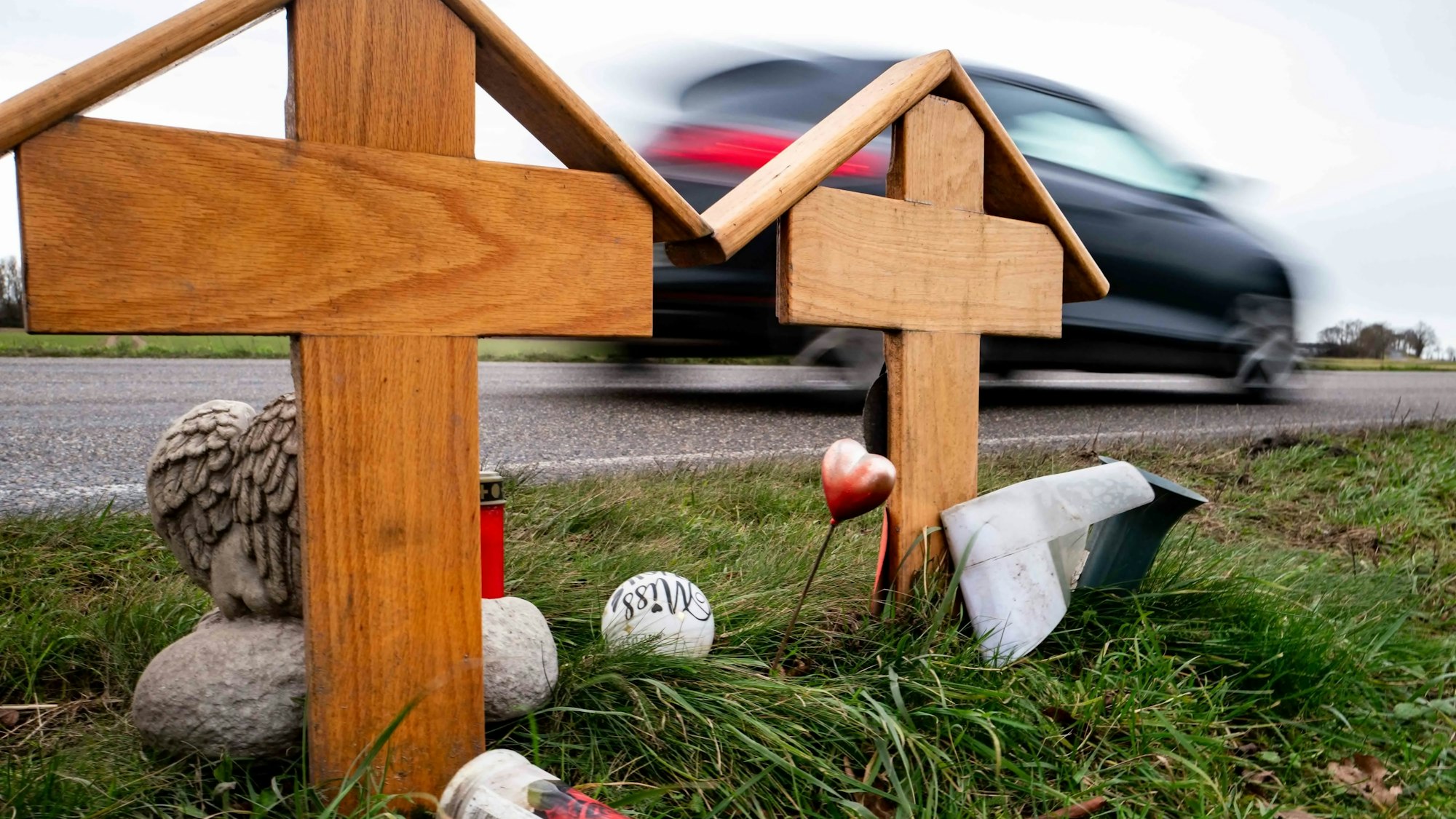 Das Bild zeigt zwei Holzkreuze an der L163. Im Hintergrund fährt ein Auto vorbei.