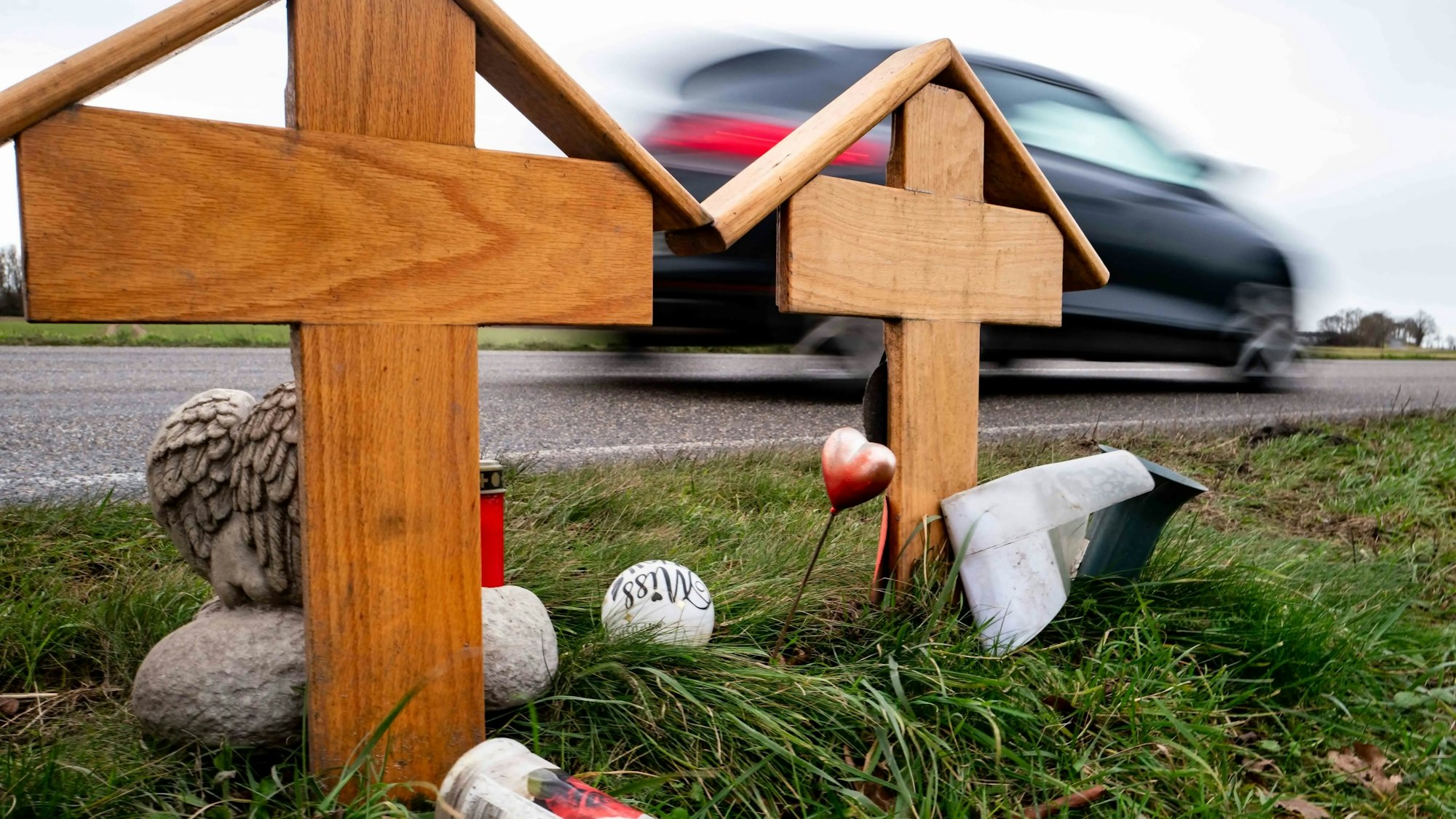Das Bild zeigt zwei Holzkreuze an der L163. Im Hintergrund fährt ein Auto vorbei.