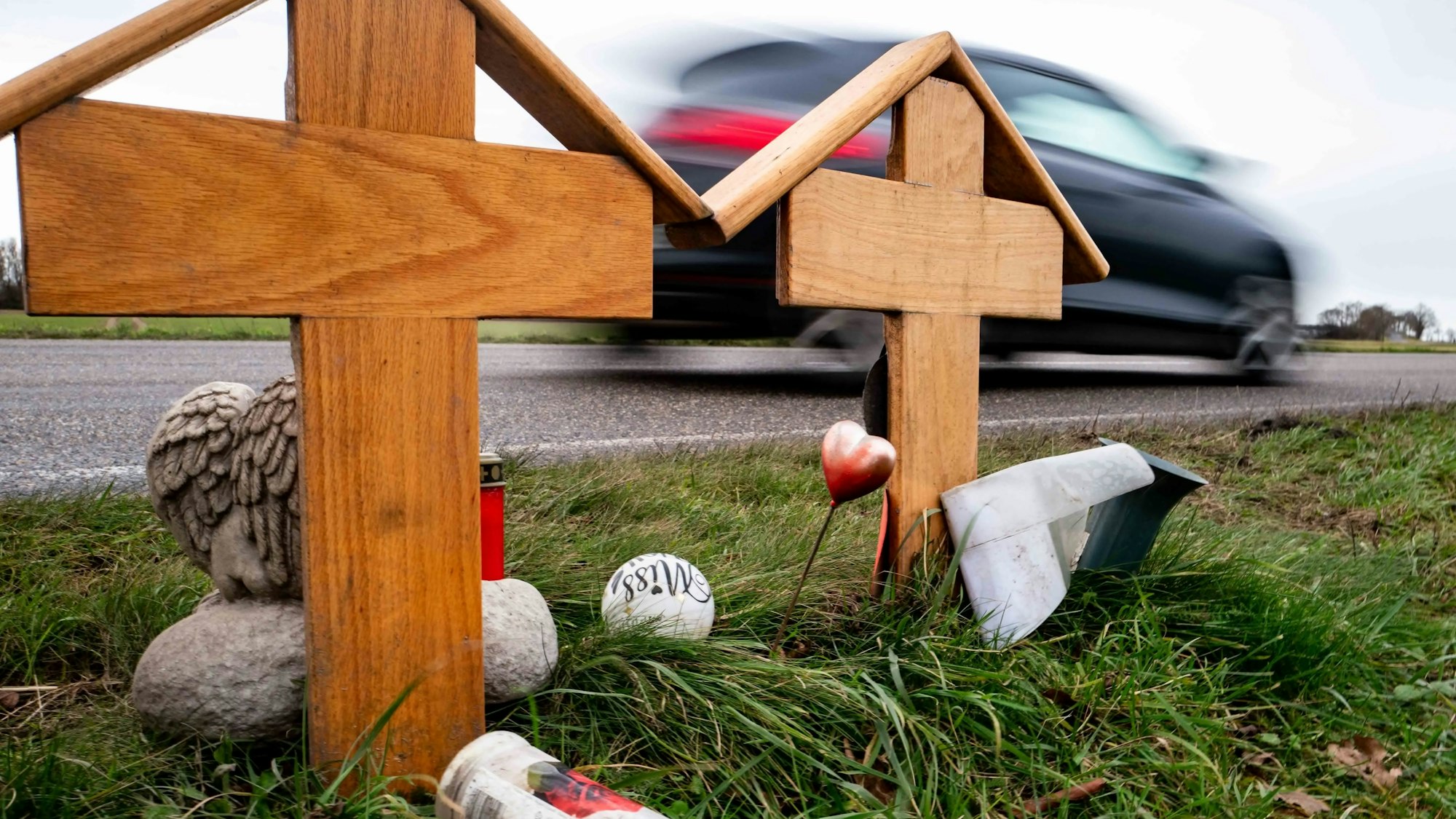 Zwei Holzkreuze erinnern an den Unfall zwischen Weilerswist und Metternich am Karnevalssonntag des vergangenen Jahres. Ein schwarzes Auto fährt auf der Straße daran vorbei.
