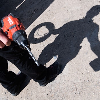 Ein Auszubildender eines Elektroinstallationsbetriebes wirft mit aufgerollten Kabel und einem Akkuschrauber einen Schatten.