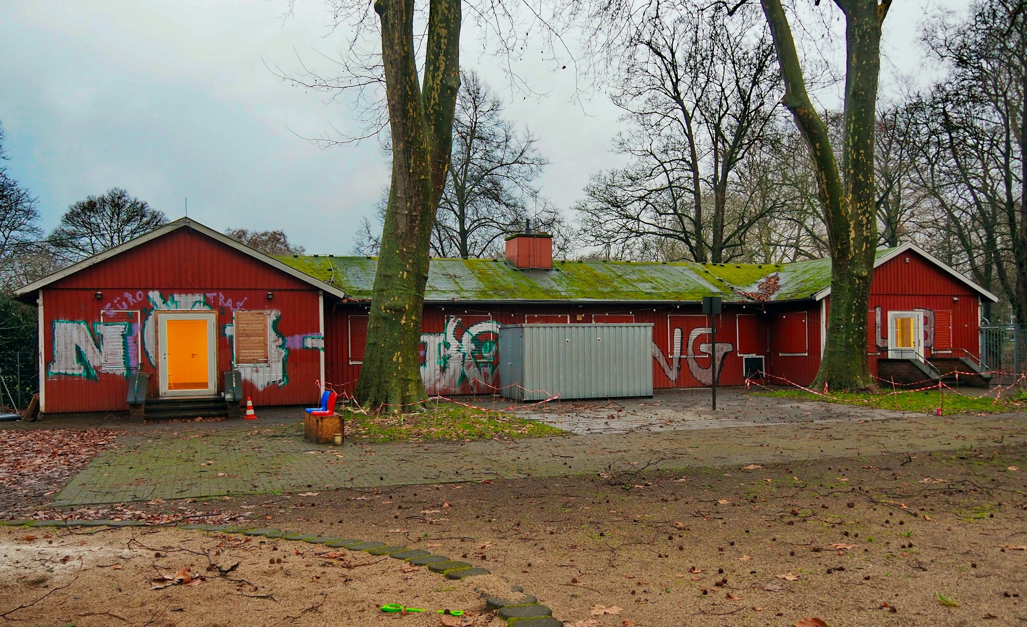 Rückansicht von einem niedrigen langgezogenen Holzgebäude, das rot gestrichen ist. Große Bäume stehen vor dem Gotlandhaus.