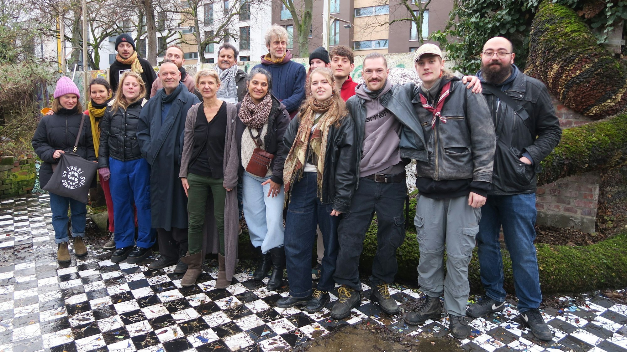 Eine Gruppe Menschen steht in einem Hof auf einem schwarz-weiß-gefliesten Boden.