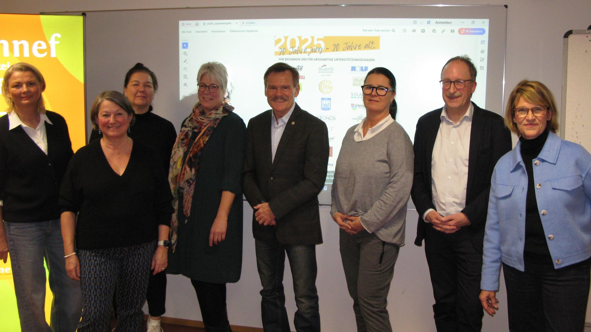 Sechs Frauen und zwei Männer stehen nebeneinander vor einer Präsentationsleinwand.