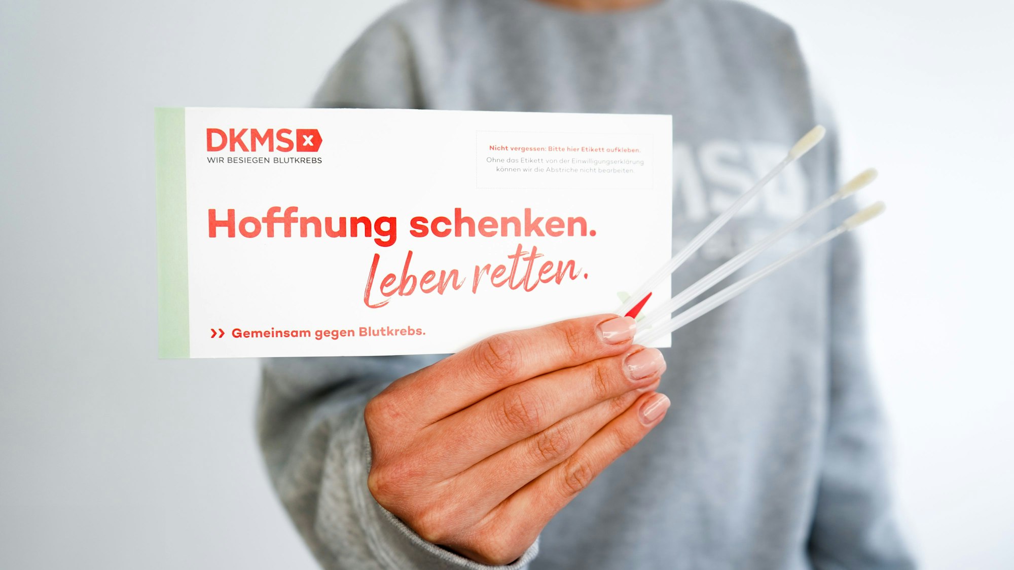 Eine Frau hält eine Broschüre von DKMS und drei Wattestäbchen.