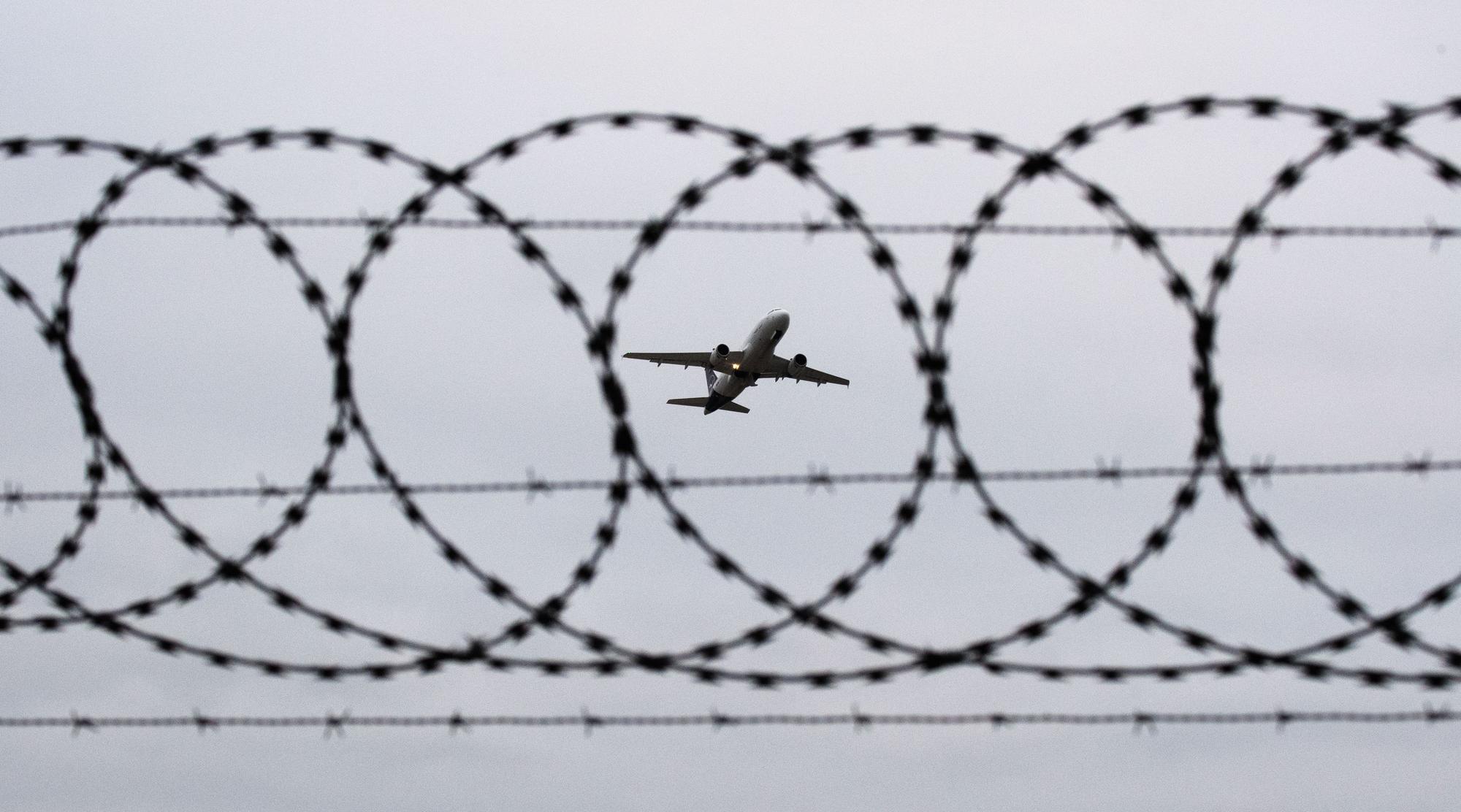 ARCHIV - 06.01.2020, Niedersachsen, Hannover: Ein Flugzeug startet - fotografiert durch Stacheldraht am Flughafenzaun.