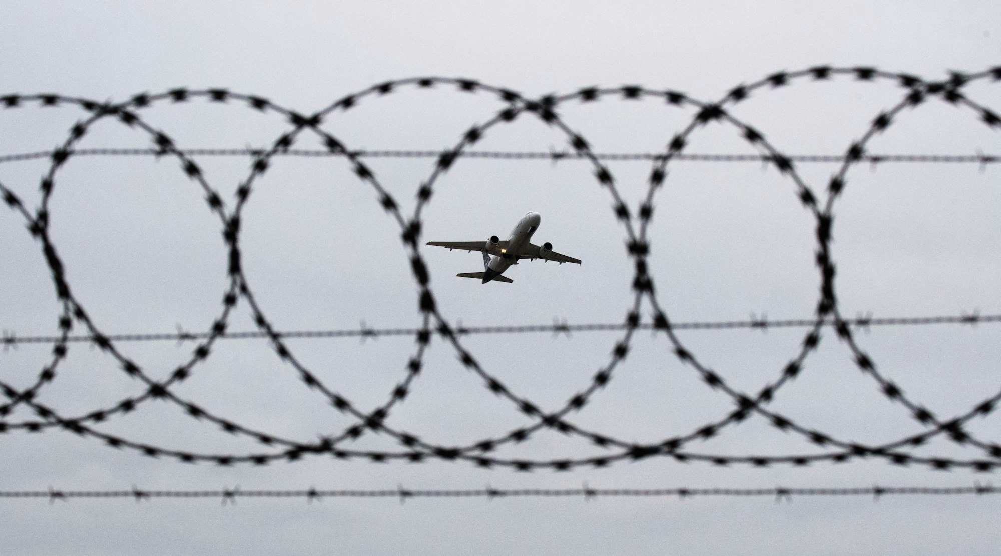 ARCHIV - 06.01.2020, Niedersachsen, Hannover: Ein Flugzeug startet - fotografiert durch Stacheldraht am Flughafenzaun.
